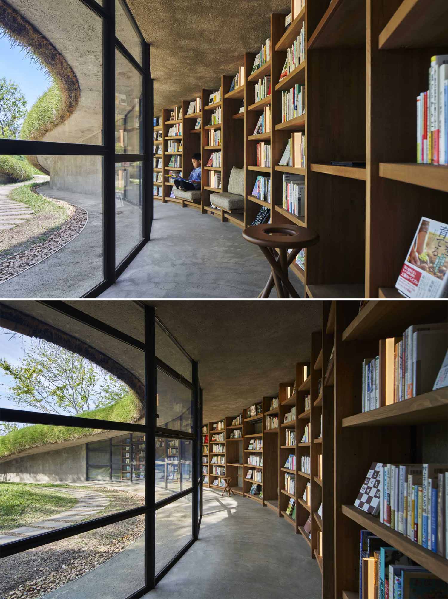 A modern library built into the earth includes a curved glass wall and bookshelves that wrap around the wall.