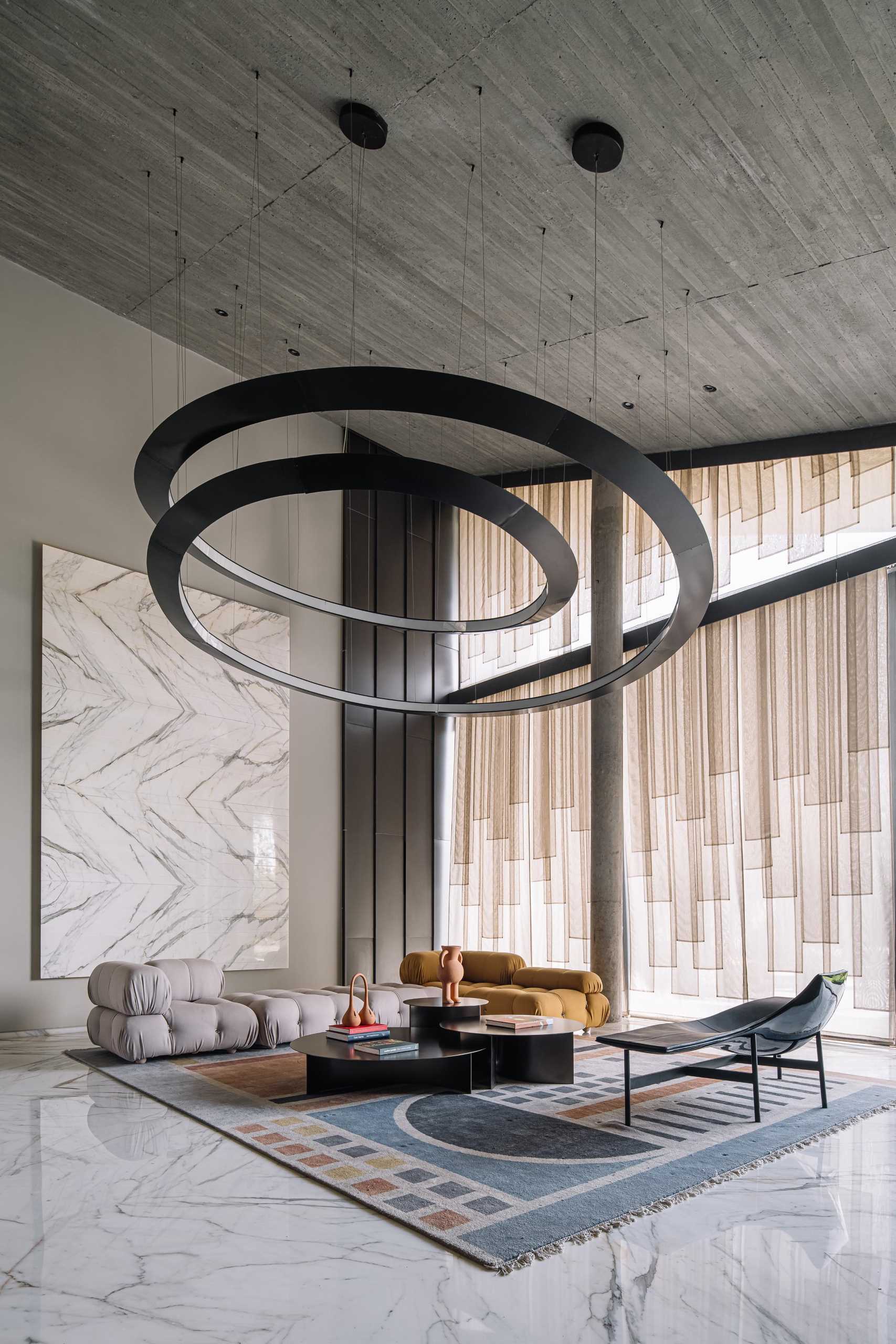 A modern living room with high ceiling, sculptural lighting, and floor-to-ceiling windows.