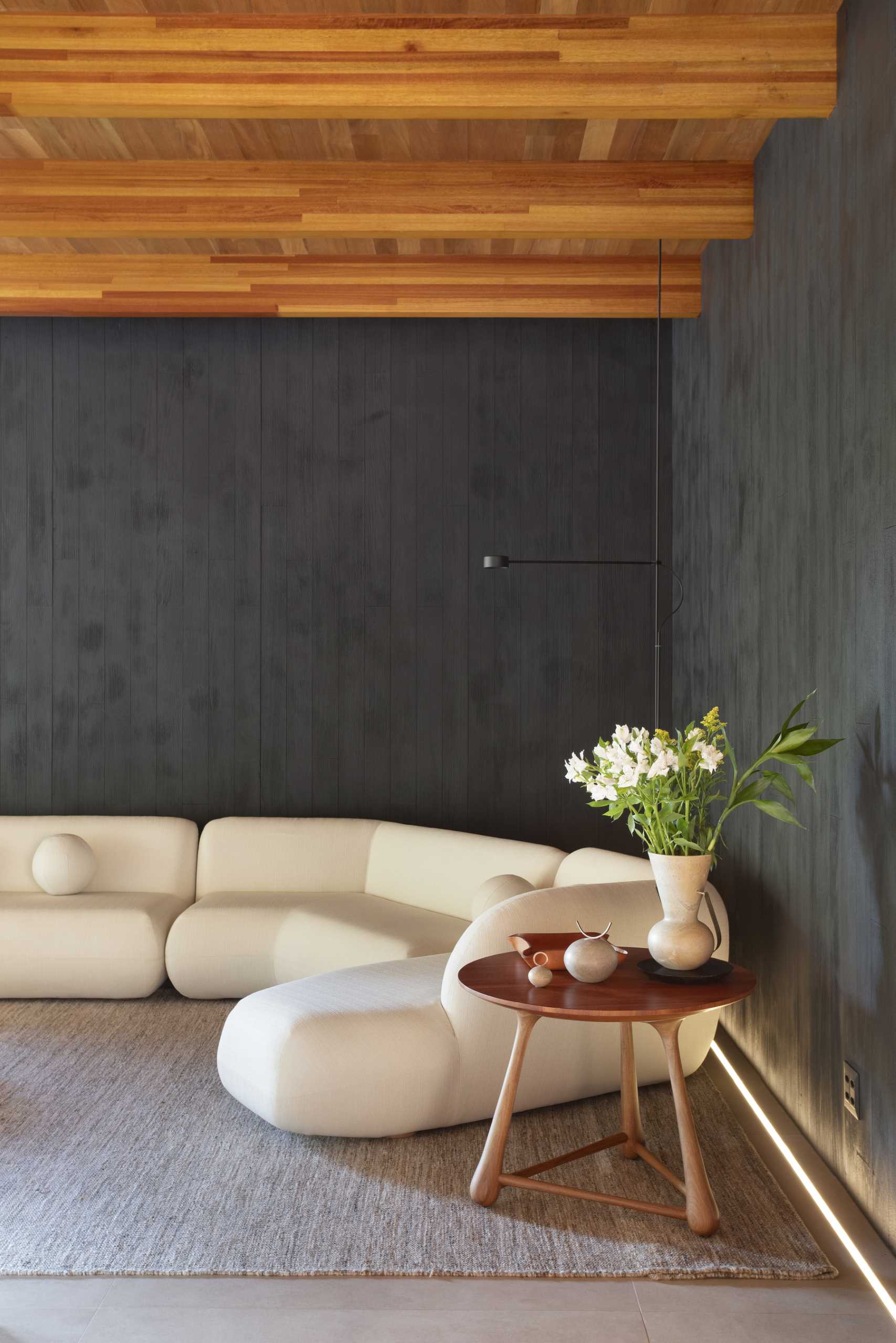 In this modern TV room, there's a dark wood accent wall made from Muiracatiara wood slats finished with a Shou Sugi Ban treatment.