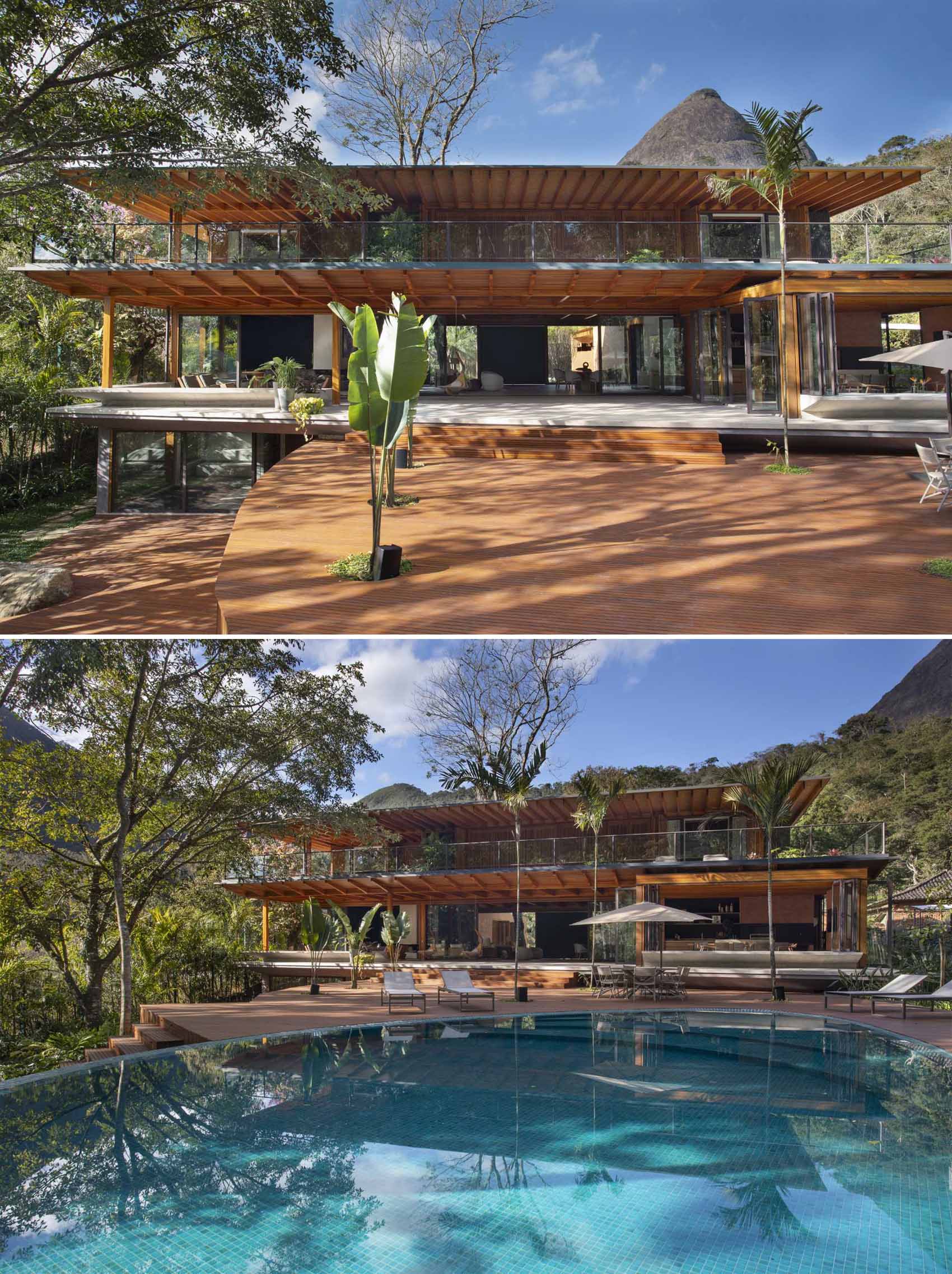 This modern house has steps that lead down from the patio to the wood deck, which has openings for plants to grow through. The deck wraps around the swimming pool, both of which have tree views.