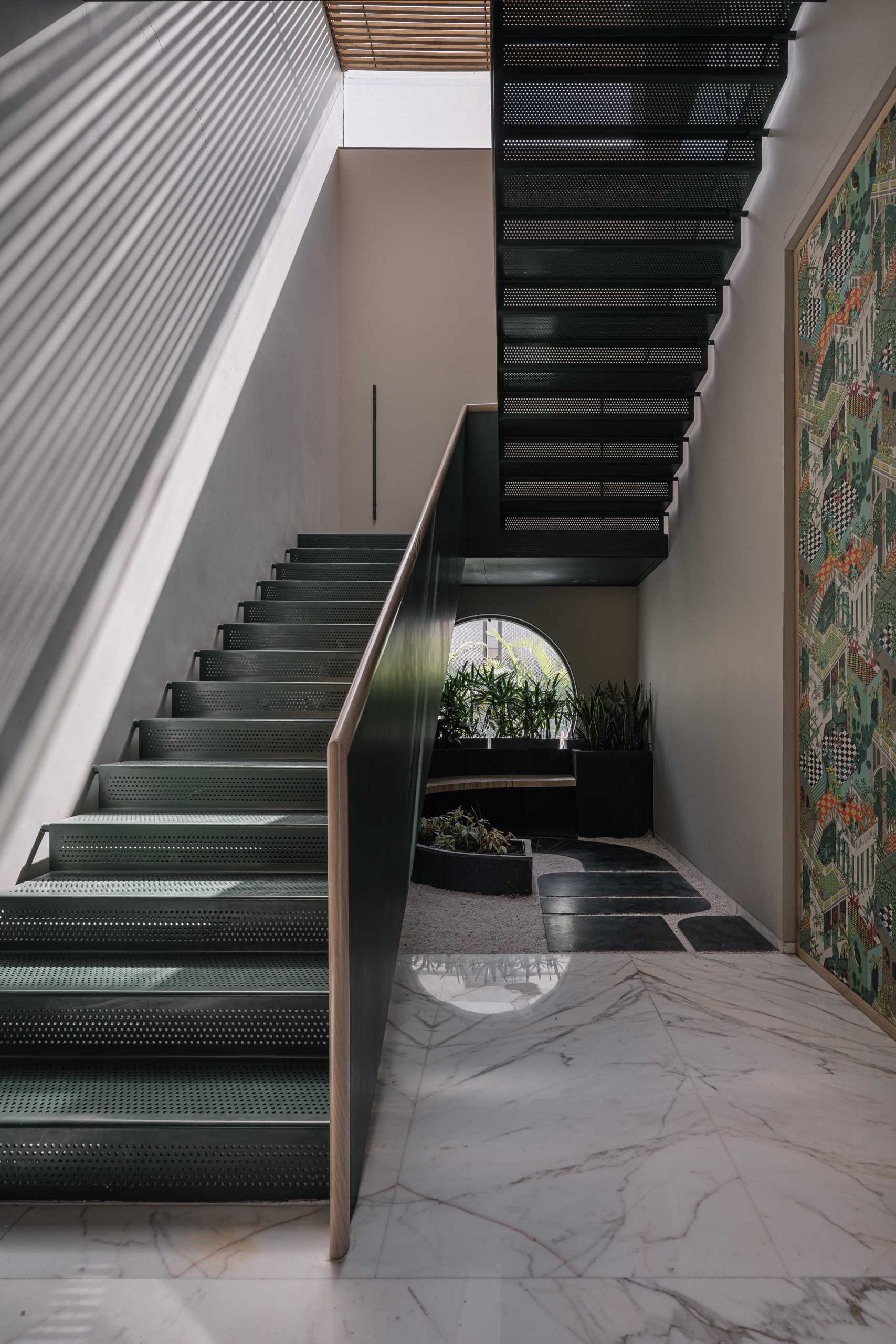 Metal stairs with a wood handrail are lit by a skylight above, while below, there's a seating area tucked in near a round window.