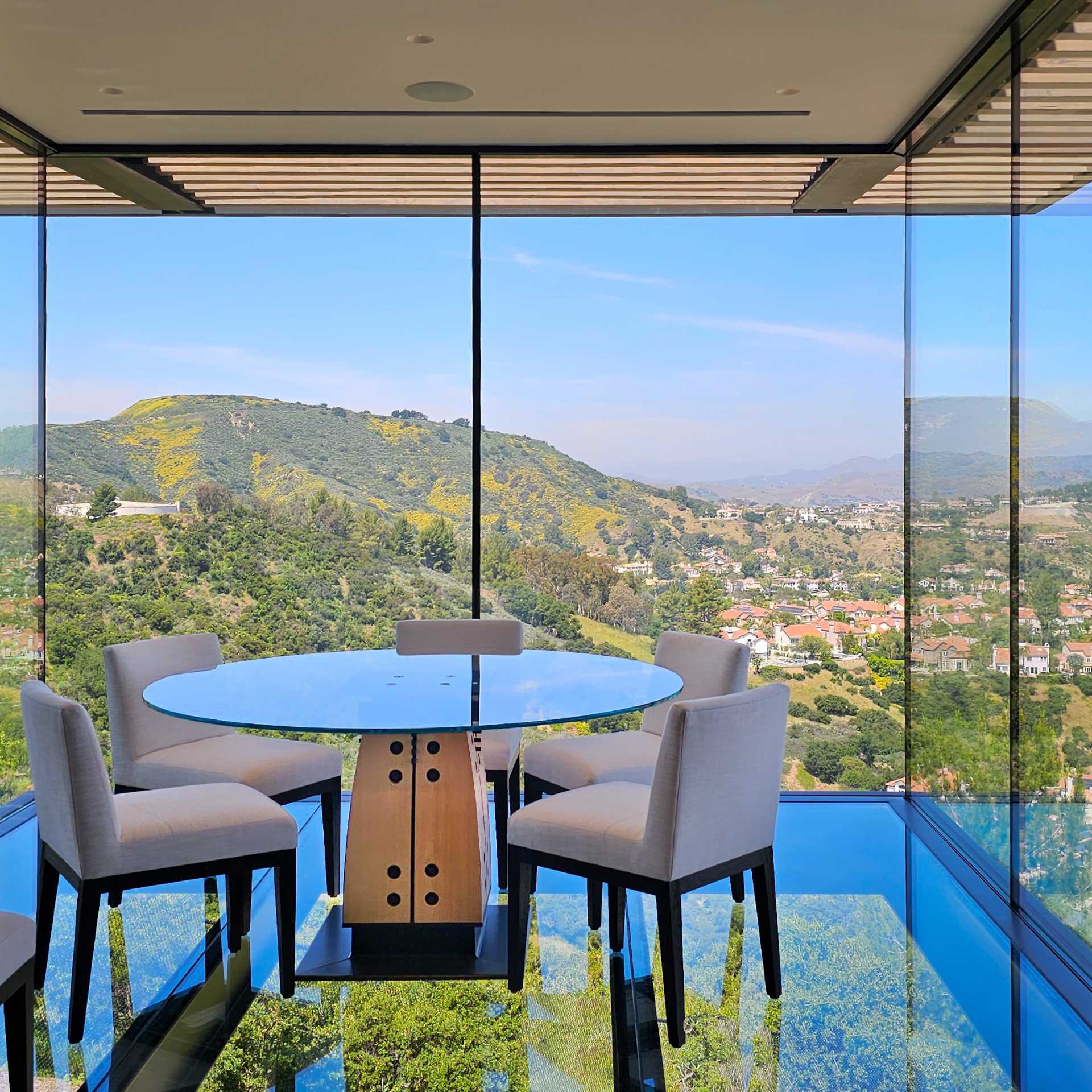 A modern cantilevered dining room with glass walls and floor.