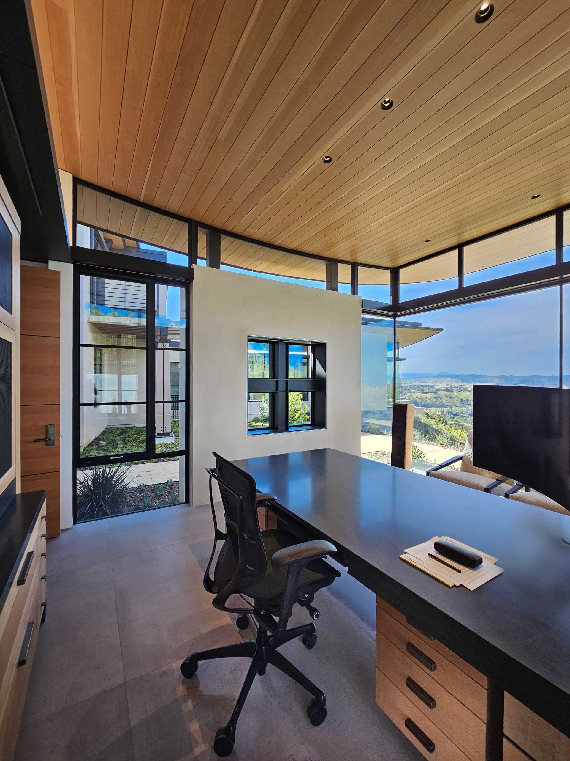 Un birou modern de acasă, cu ferestre din podea până în tavan, oferă lumină naturală și vederi extinse.