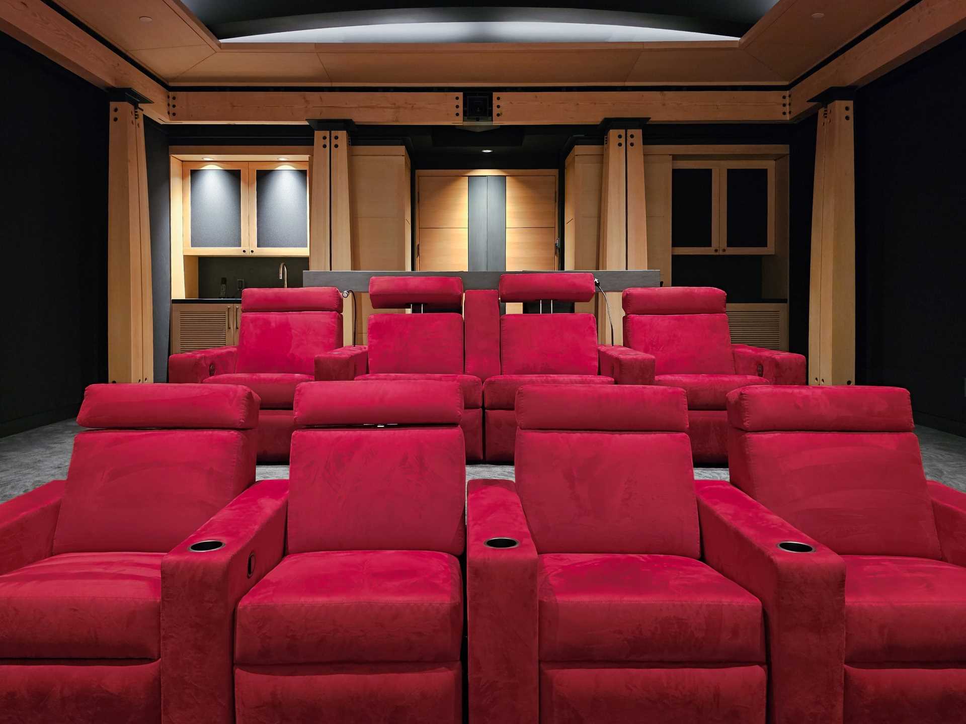 In this home theater, bright red chairs add a pop of colour to the black and wood interior.