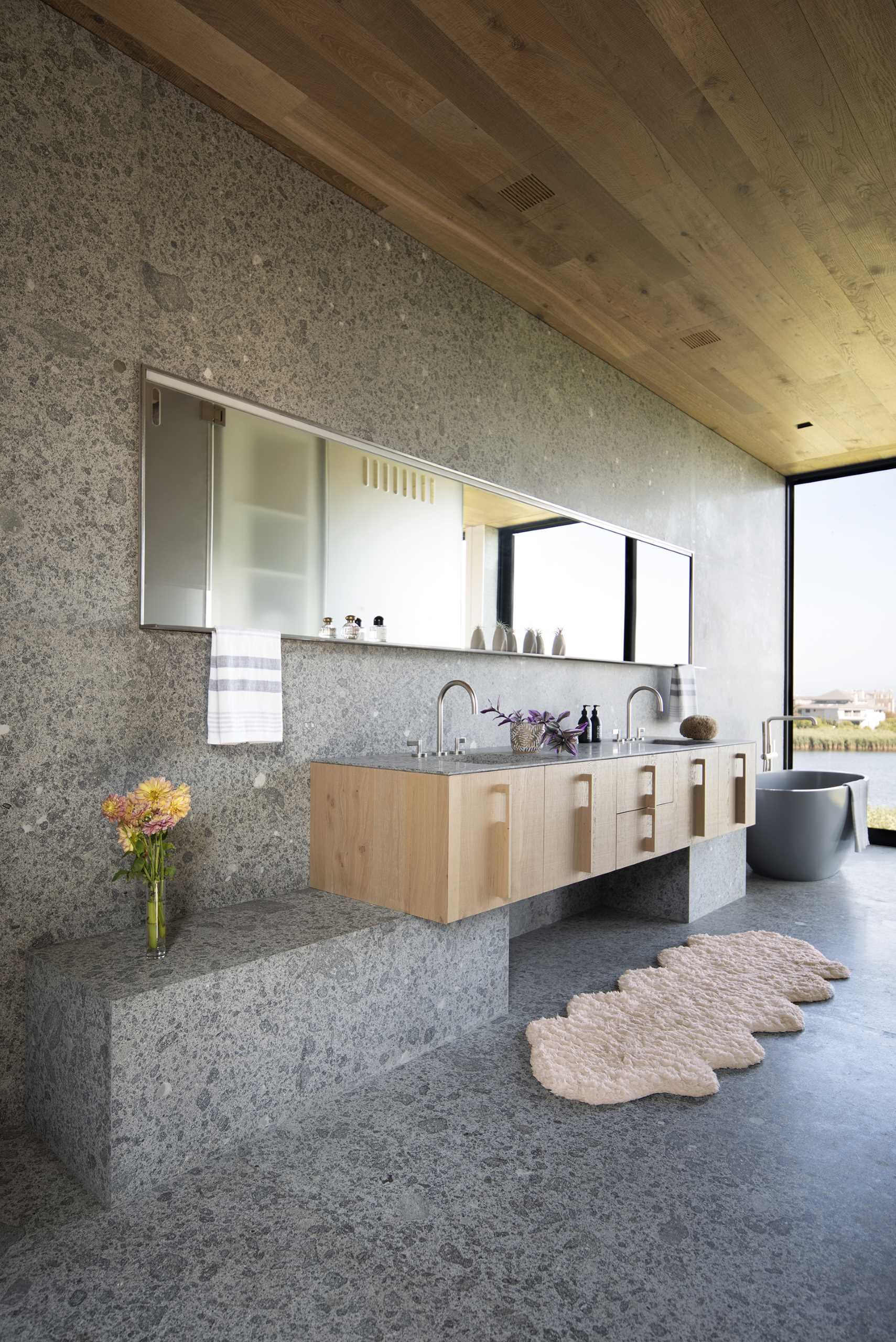 In this modern bathroom, a custom-designed vanity lines the wall, while the wood ceiling matches the other wood ceilings throughout the home.