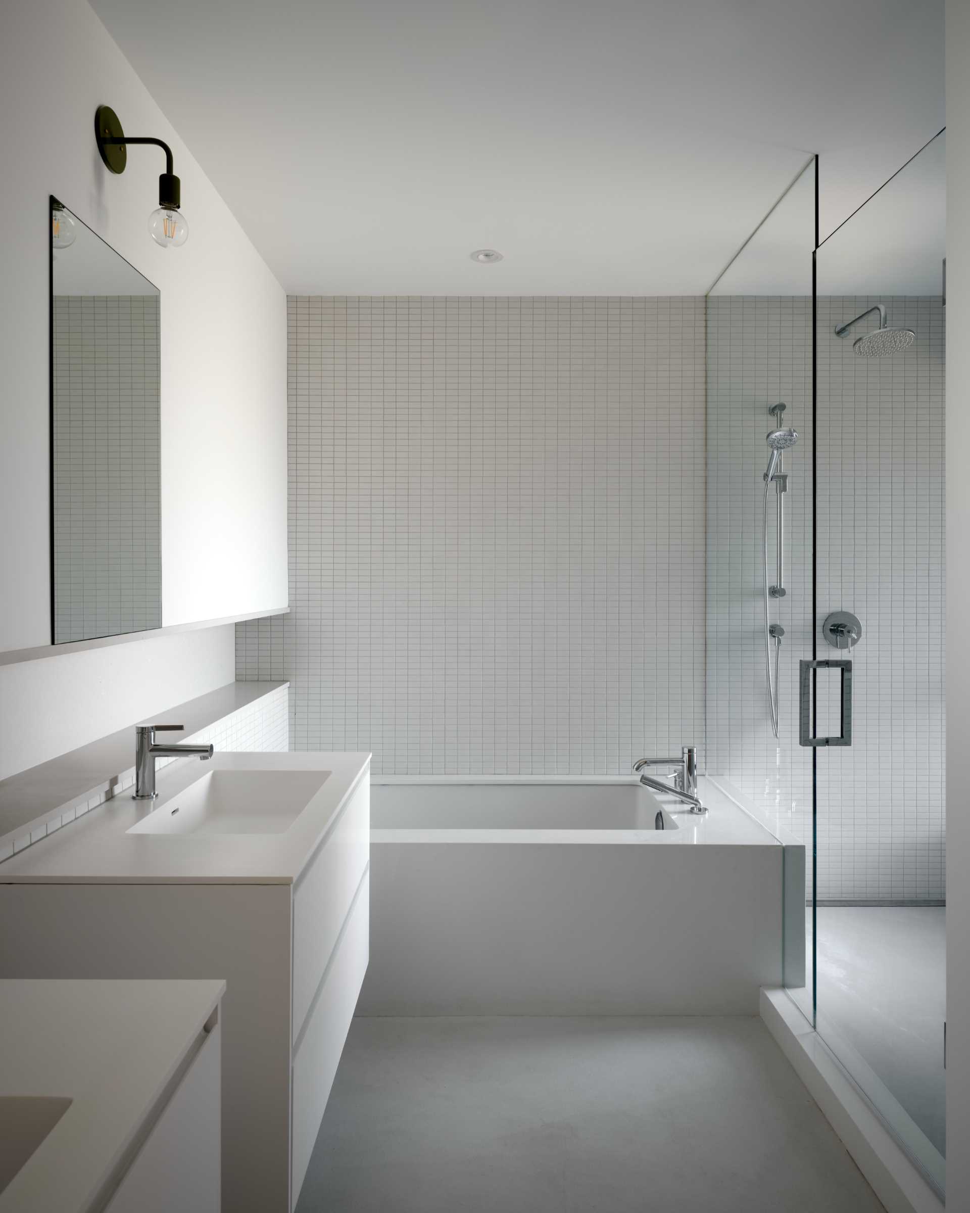 A modern bathroom has a built-in bathtub with a wall of tiles that continue through to the s،wer.
