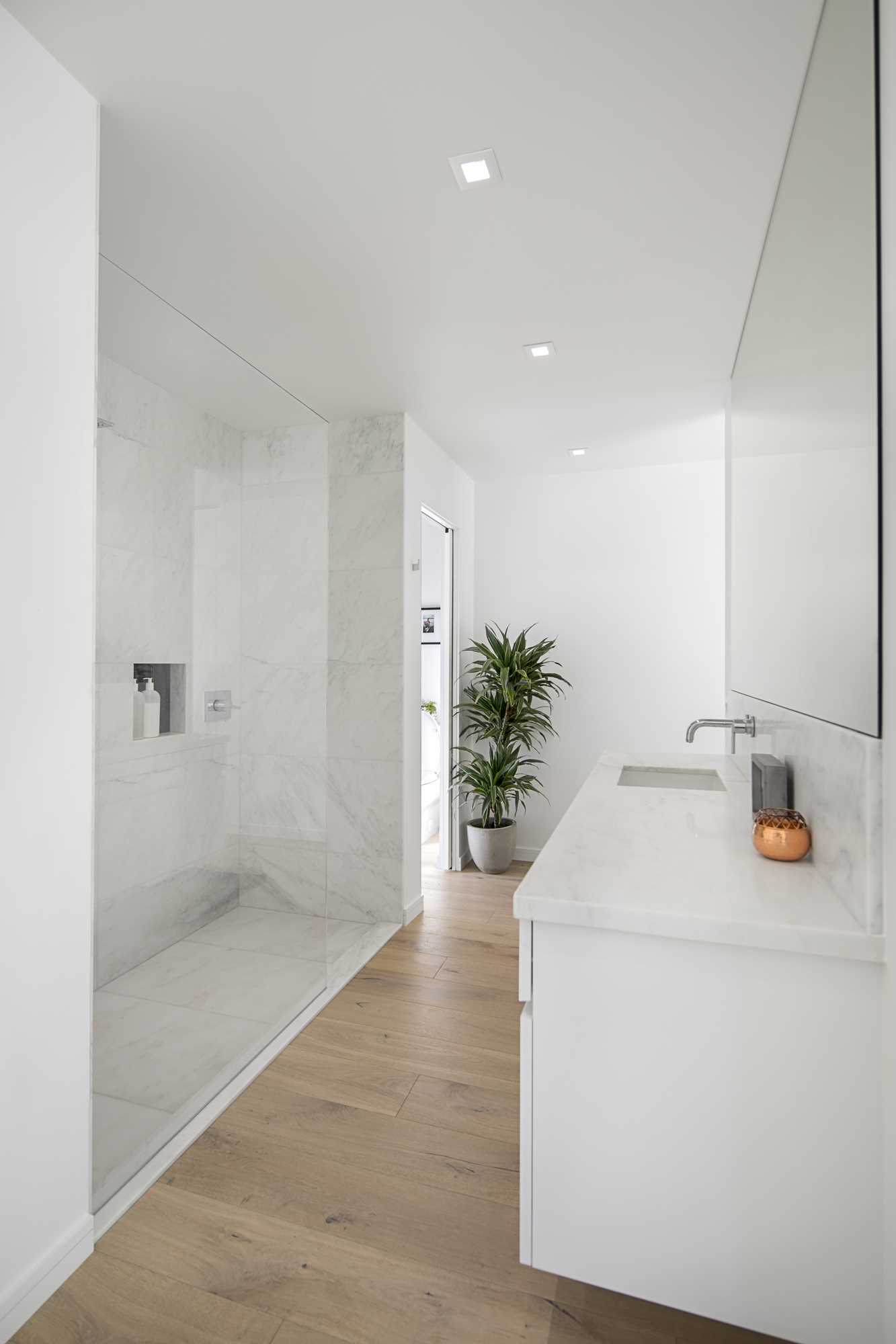 In this modern bathroom, there's a large glass-enclosed walk-in shower positioned opposite the white vanity.