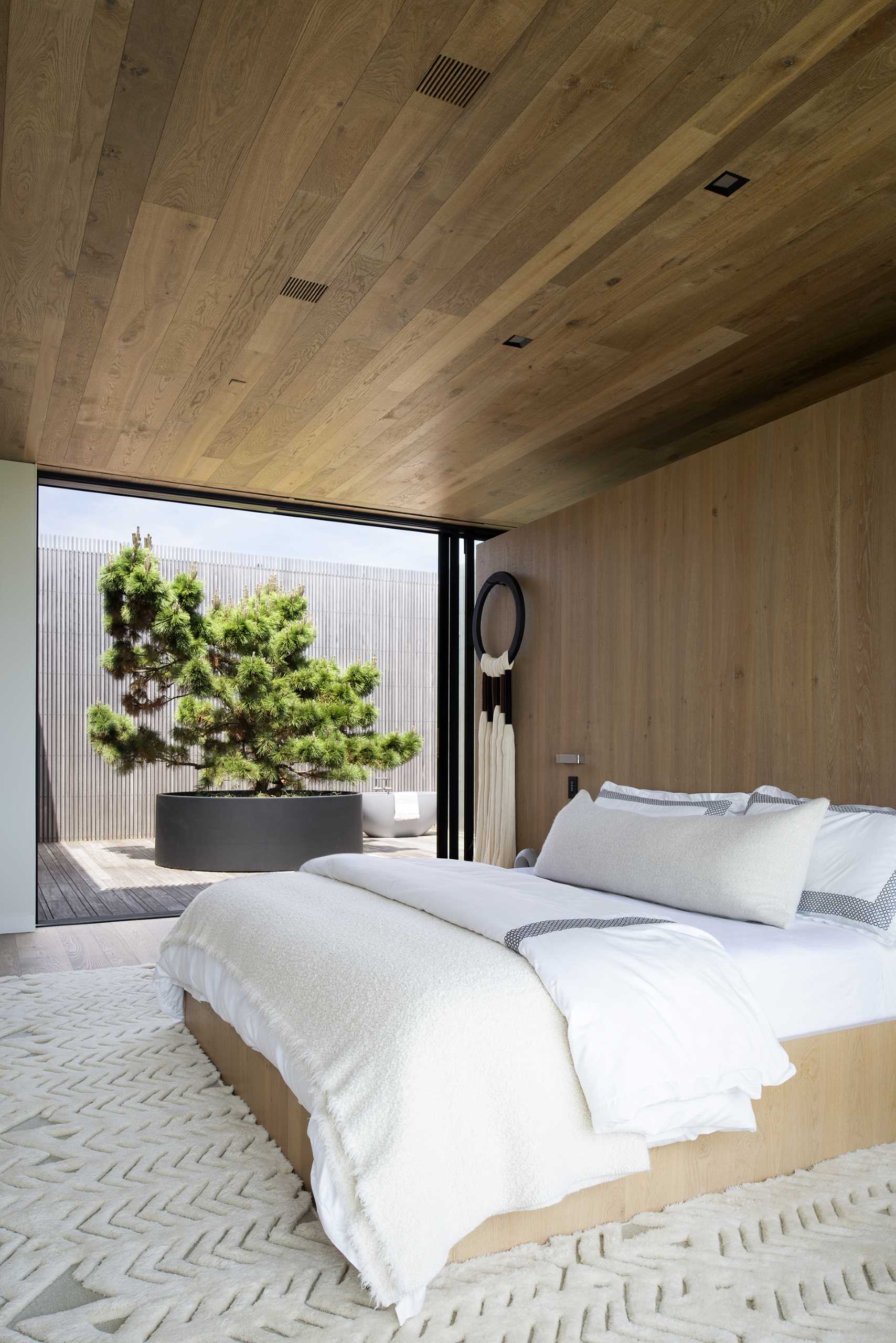 A modern bedroom with wood ceilings and a wood accent wall.