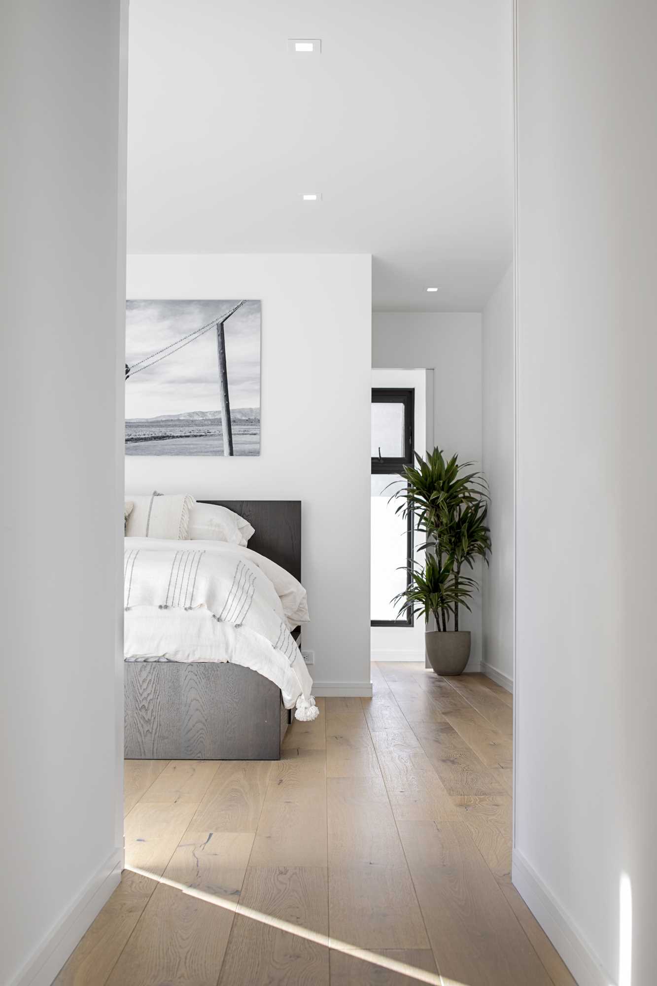 Acest dormitor are un design minimal, cu pereți albi, în timp ce podeaua din lemn adaugă un sentiment de căldură spațiului.