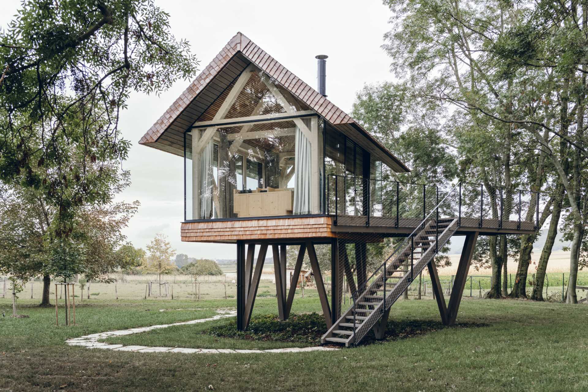 A modern elevated cabin with glass walls, a bed, a bar, and a fireplace.