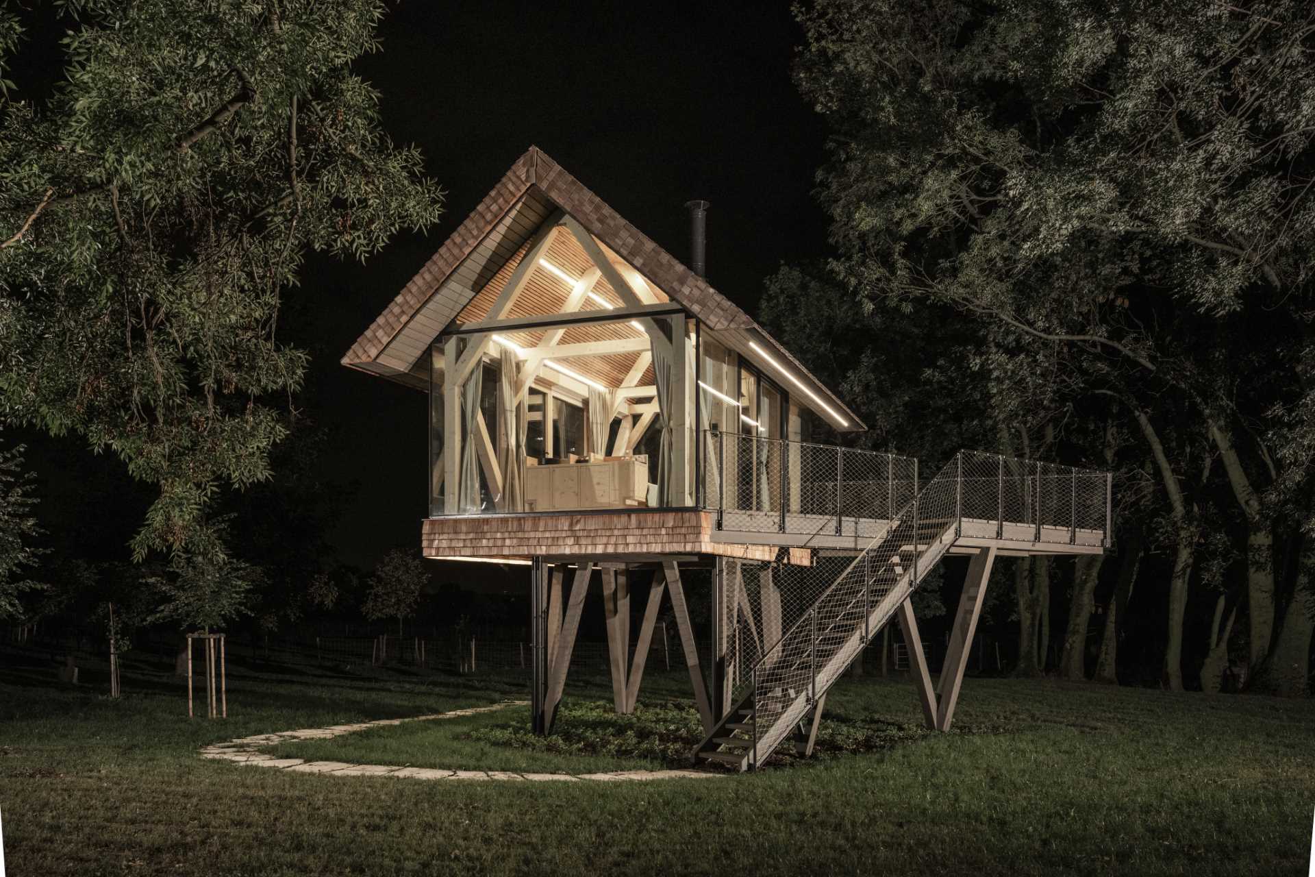 A modern elevated cabin with glass walls, a bed, a bar, and a fireplace.