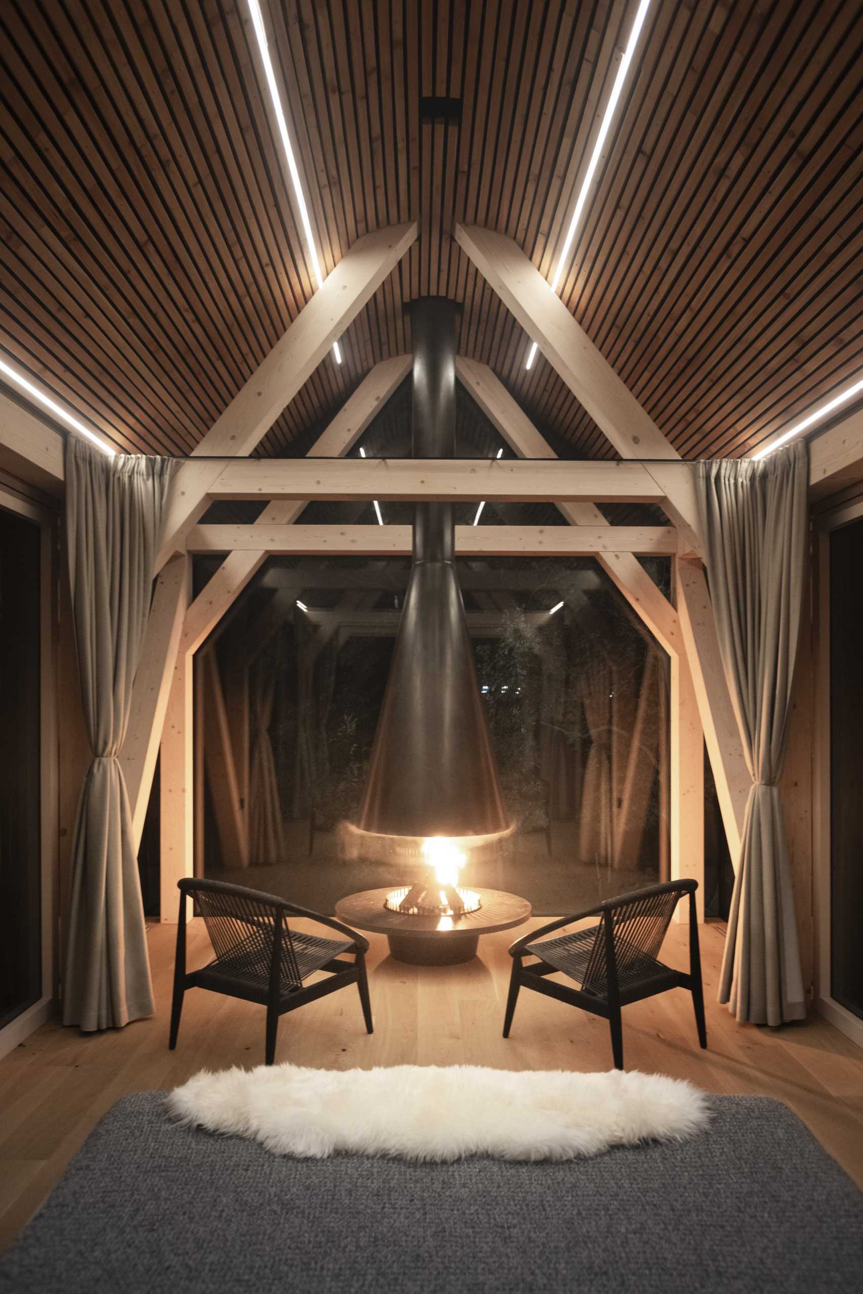 A modern elevated cabin with glass walls, a bed, a bar, and a fireplace.