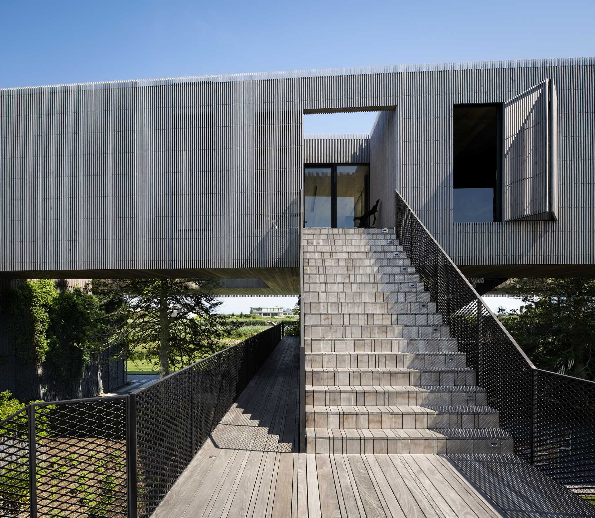 A modern house with elevated living areas, has metal stairs and wood that connect the lower levels with the upper levels.