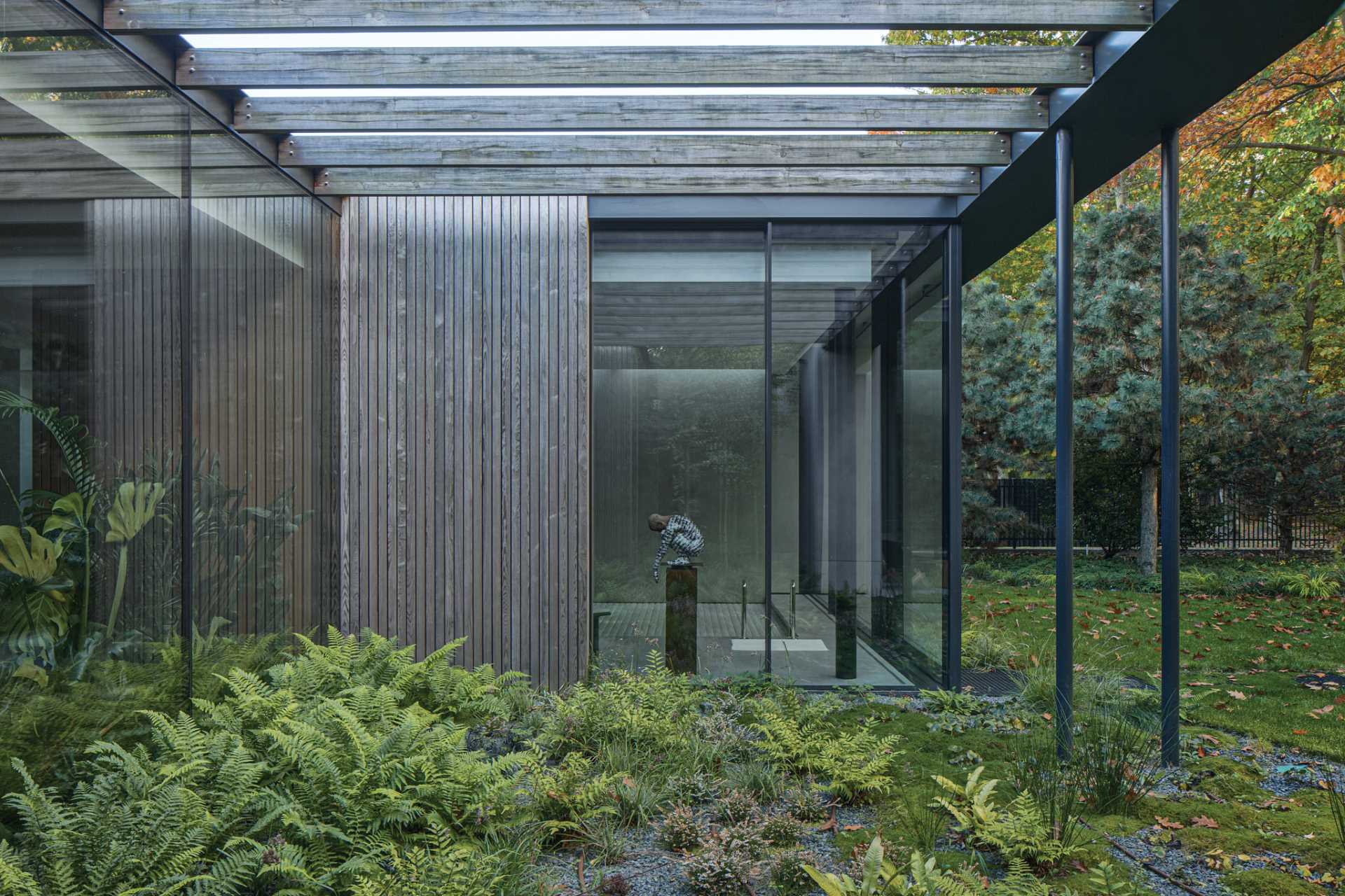 Small gardens penetrate the interior of this modern home, reaching into patios and semi-patios, appearing behind glass walls in the hall, living room, and bathroom. 