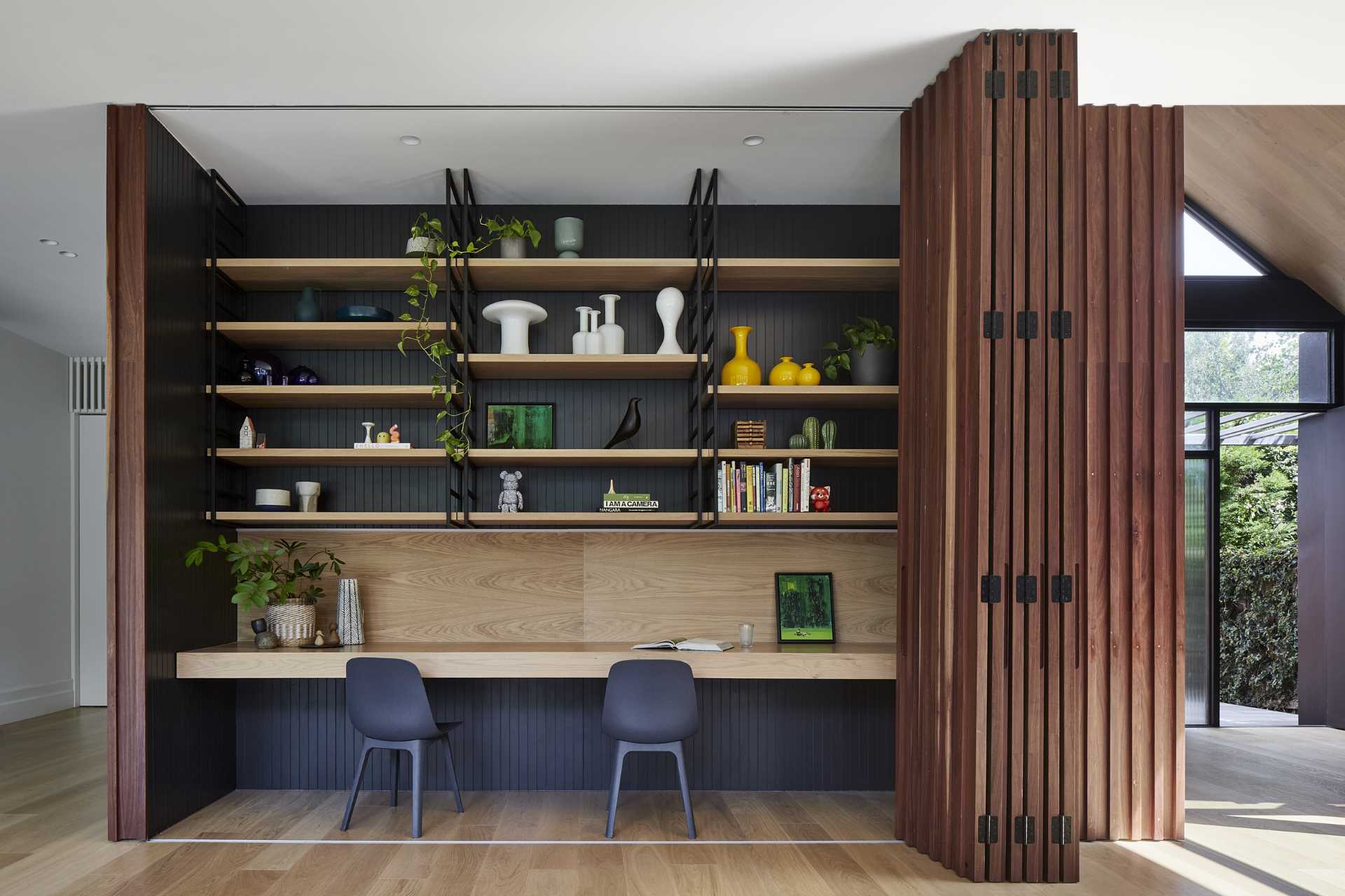 A modern home interior includes a wood accent wall that opens to reveal a hidden office for two.