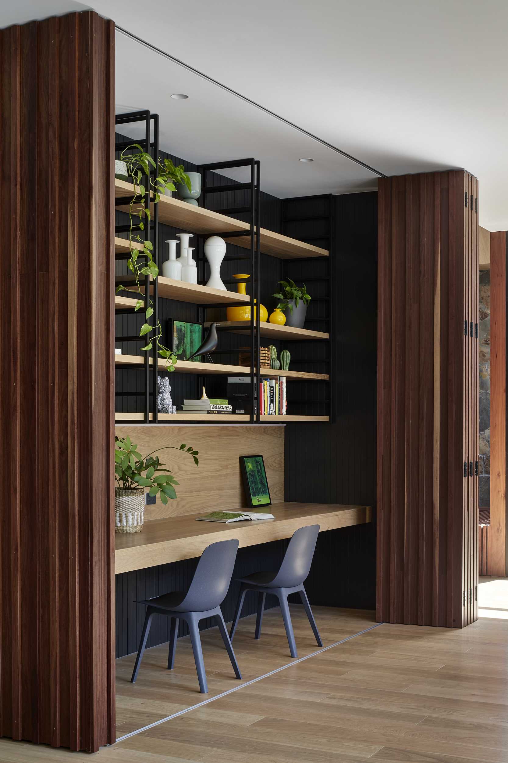 A modern home interior includes a wood accent wall that opens to reveal a hidden office for two.