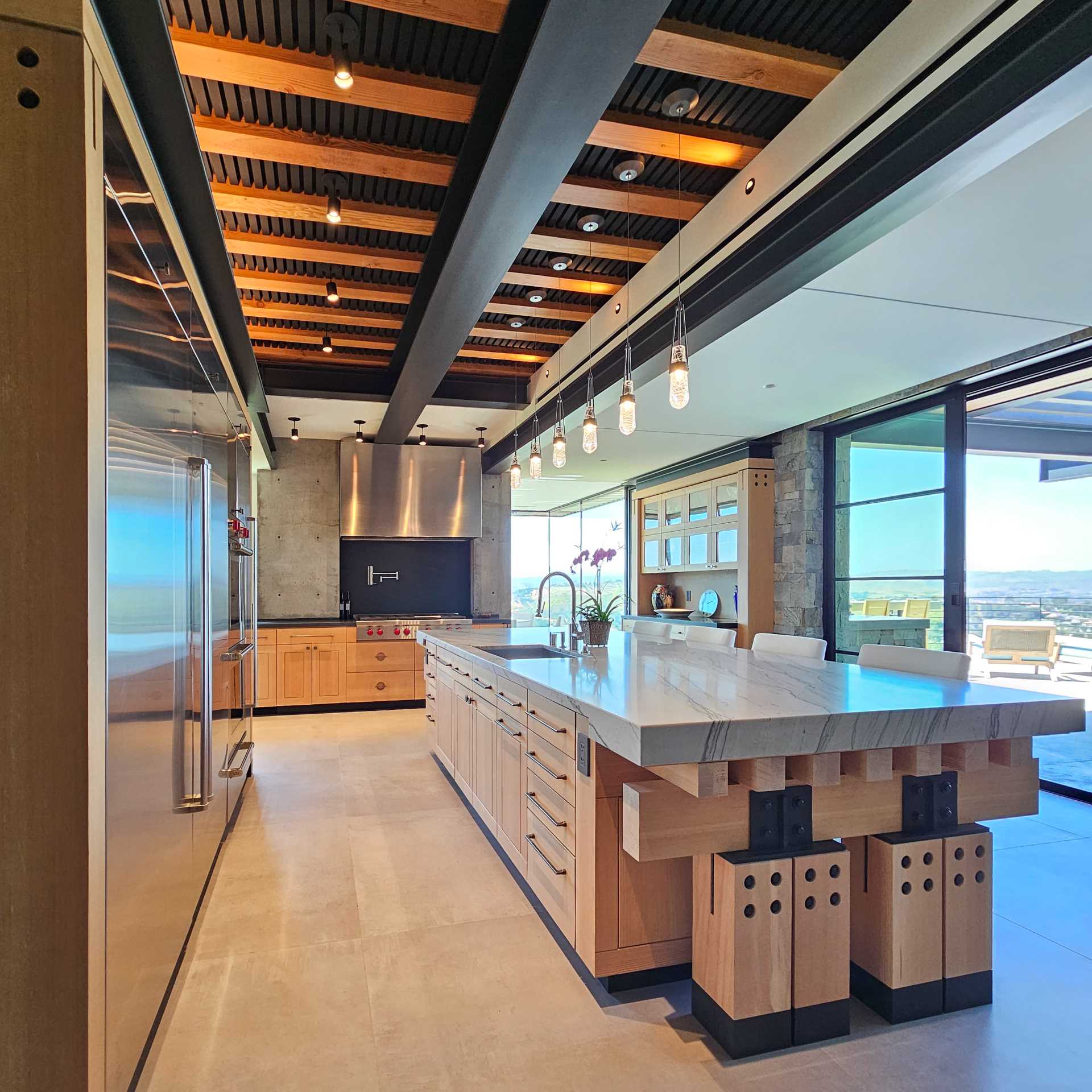 In this kitchen, an exposed concrete wall behind the professional cooktop and stainless-steel hood provides an industrial edge and grounds the space.