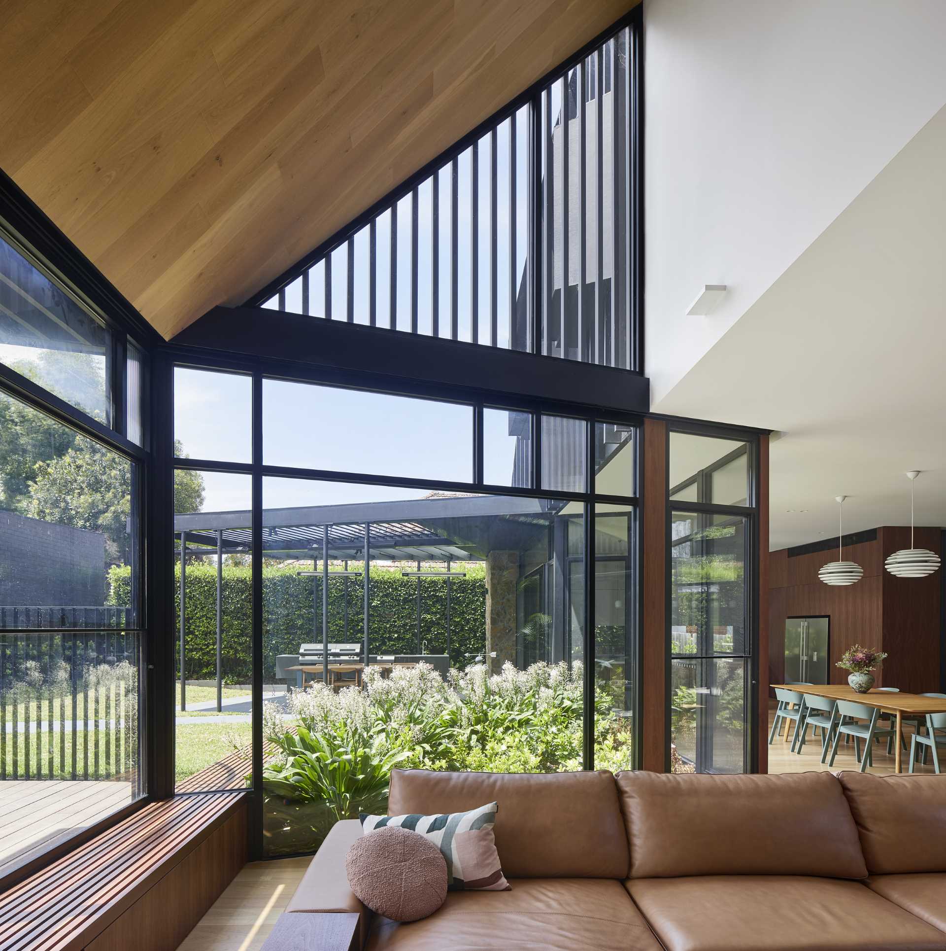 Inside this modern home, the stone wall by the swimming pool as well as the wood bench by the planter continue through to the living room which is filled with natural light from the windows.