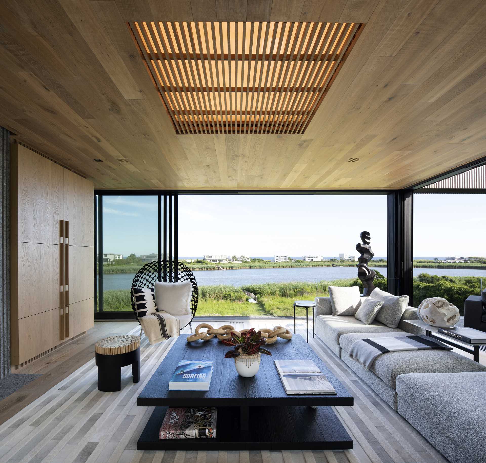 The living room of this modern house includes a wood ceiling with large operational sliding glass walls, while glass railings provide an uninterrupted view.