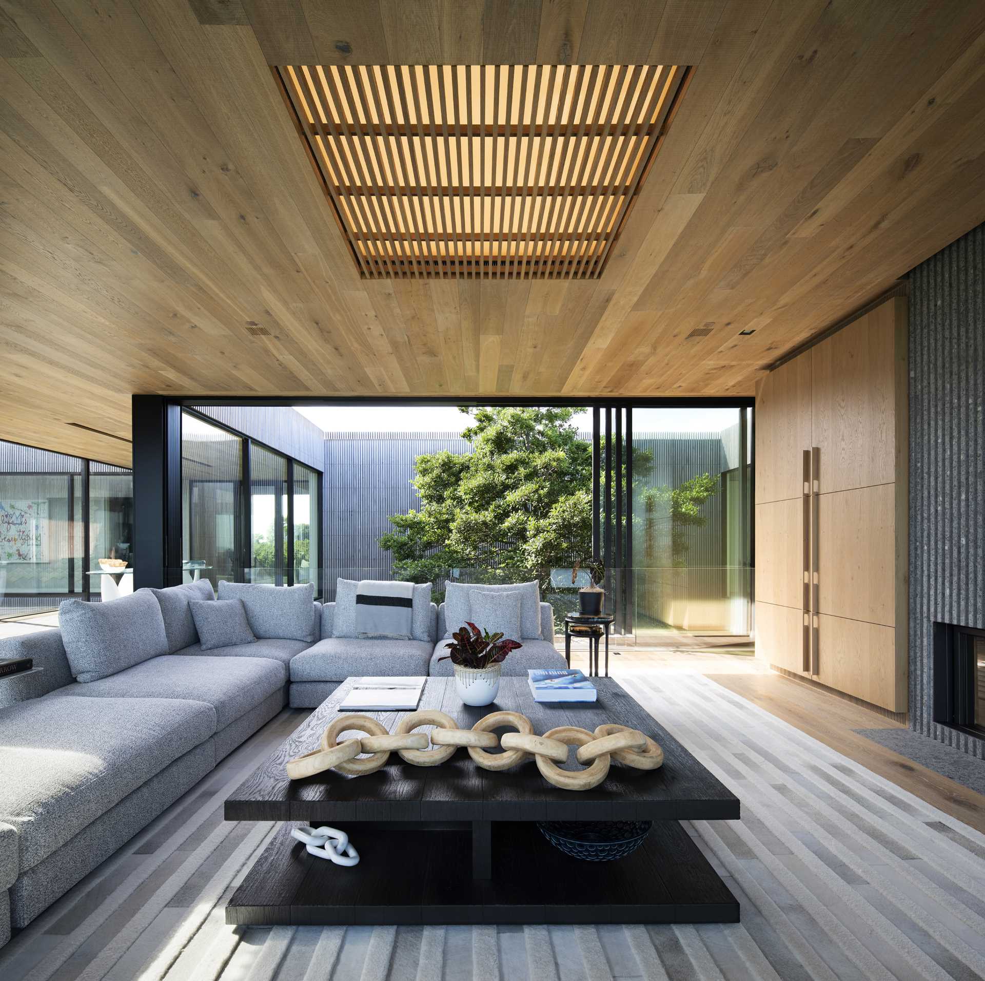 The living room of this modern house includes a wood ceiling with large operational sliding glass walls, while glass railings provide an uninterrupted view.