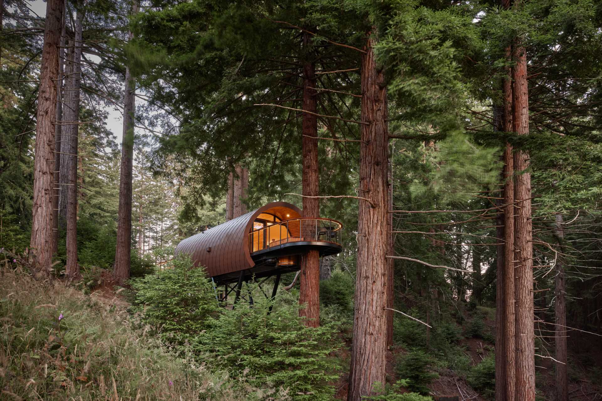 A modern treehouse that has an tubular design and is wrapped in diamond-shaped metal tiles.