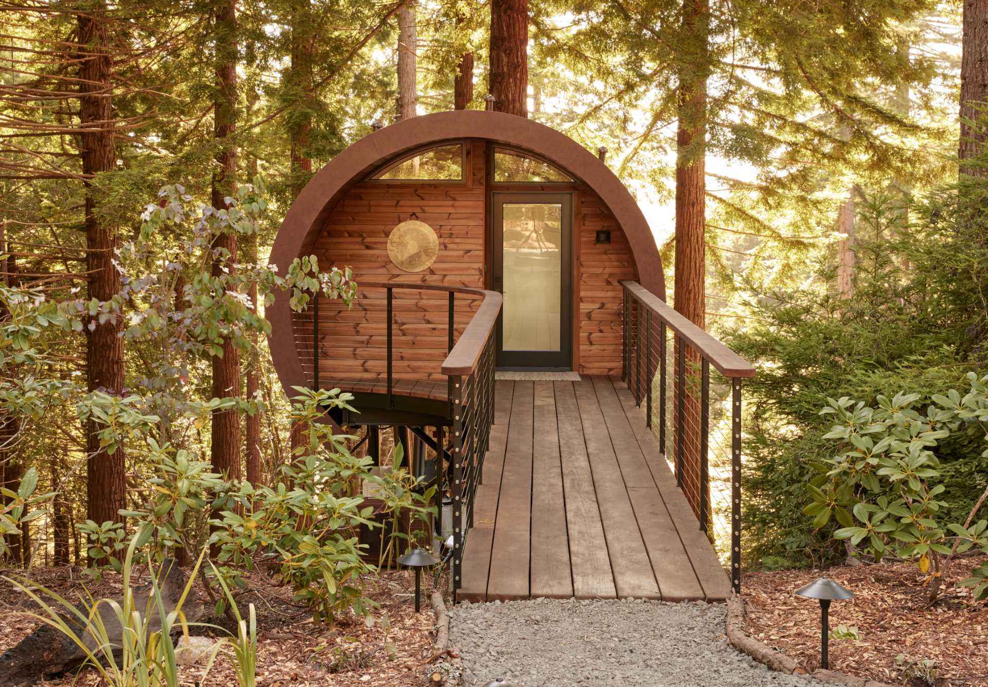 A modern treehouse cabin has a bridge that leads to the front door.