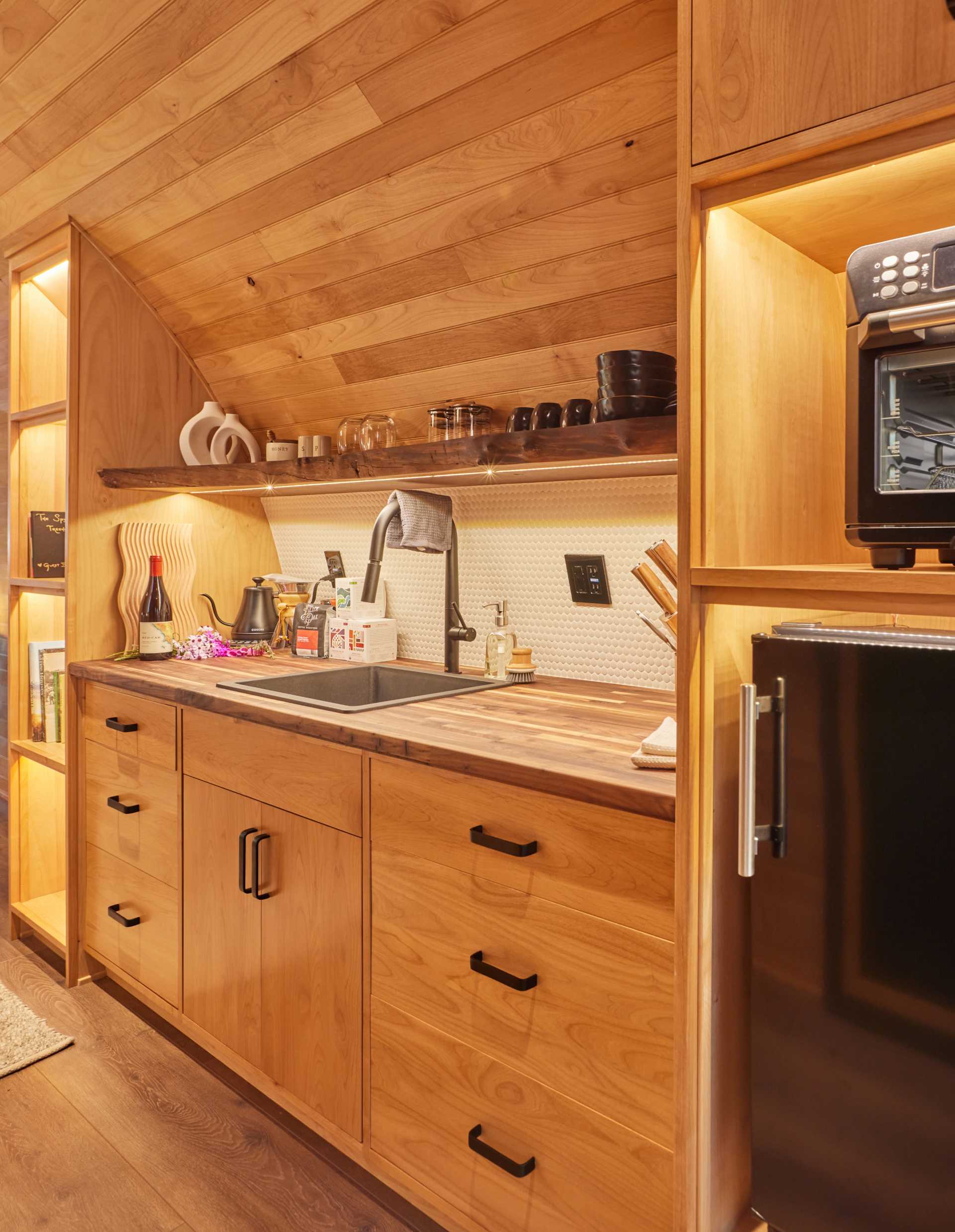 A modern treehouse with a curved design includes a bedroom area, a kitchenette, a bathroom with a shower, and a sauna.