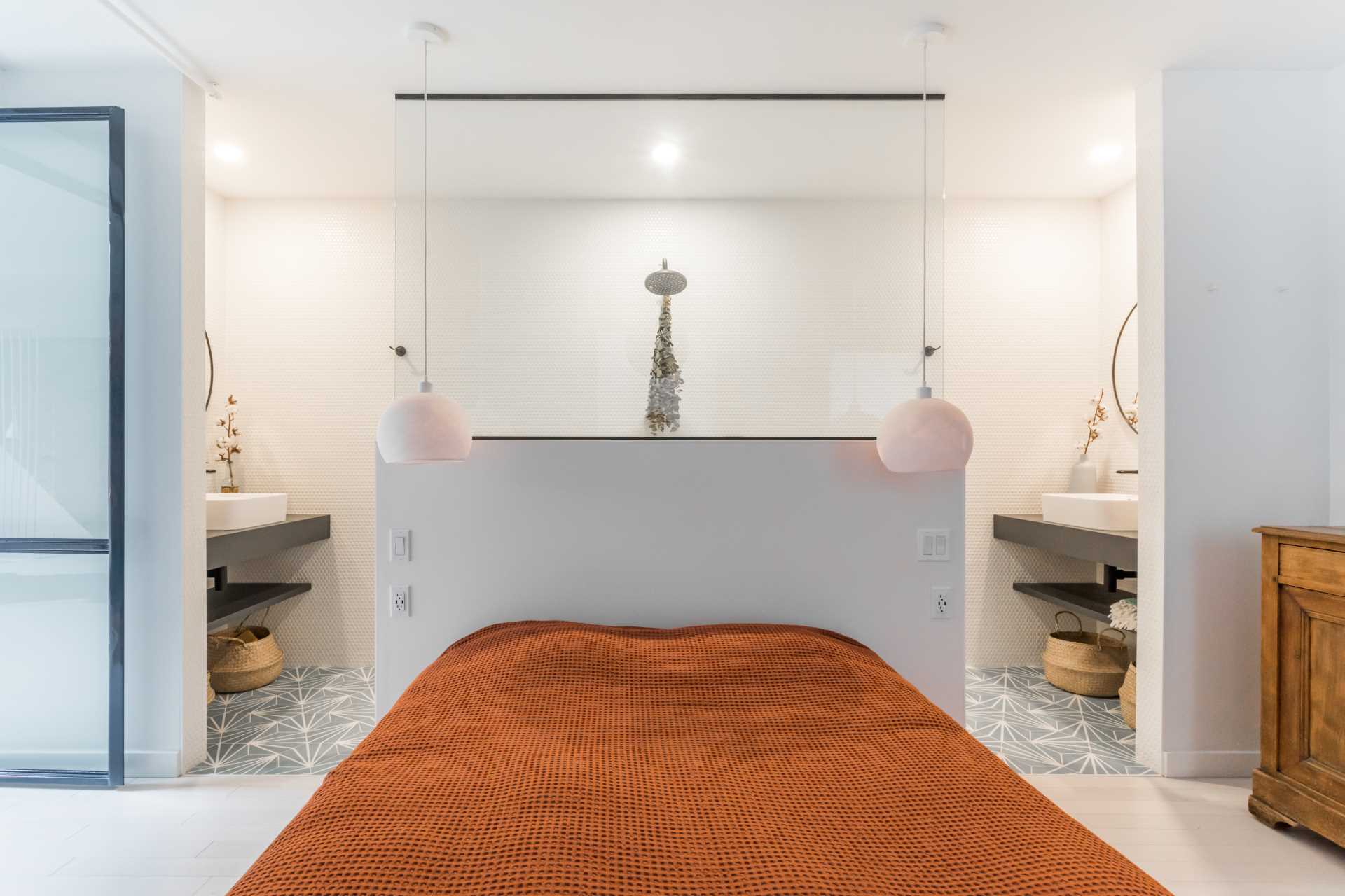 Metal-framed glass doors open to reveal the primary bedroom and bathroom. A pony wall separates the sleeping area from the bathroom, where the shower separates the two vanities.