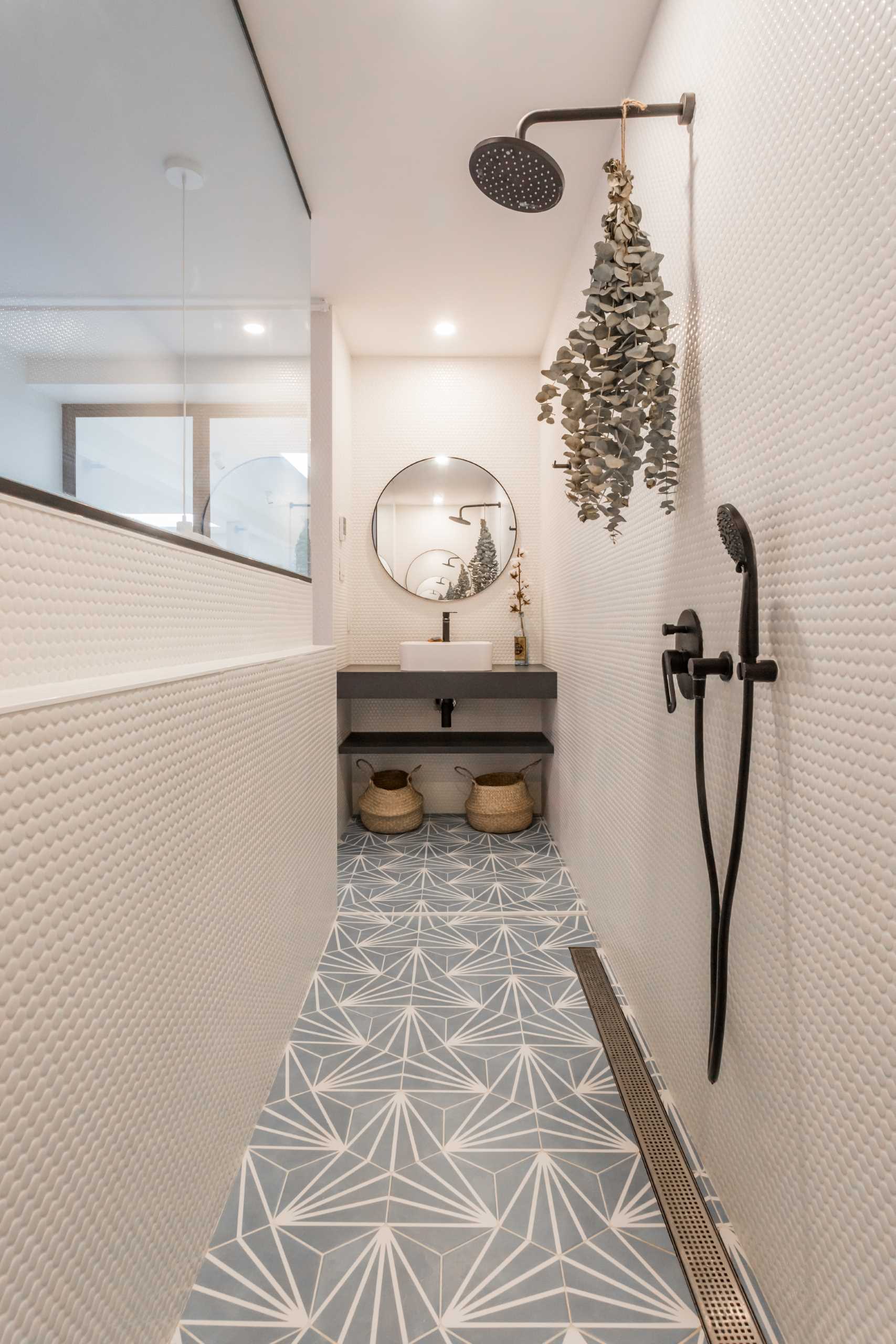 Metal-framed glass doors open to reveal the primary bedroom and bathroom. A pony wall separates the sleeping area from the bathroom, where the shower separates the two vanities.