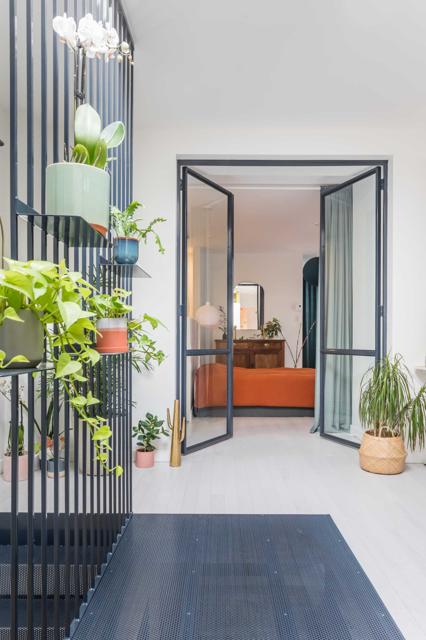 Metal-framed glass doors open to reveal the primary bedroom and bathroom. A pony wall separates the sleeping area from the bathroom, where the shower separates the two vanities.