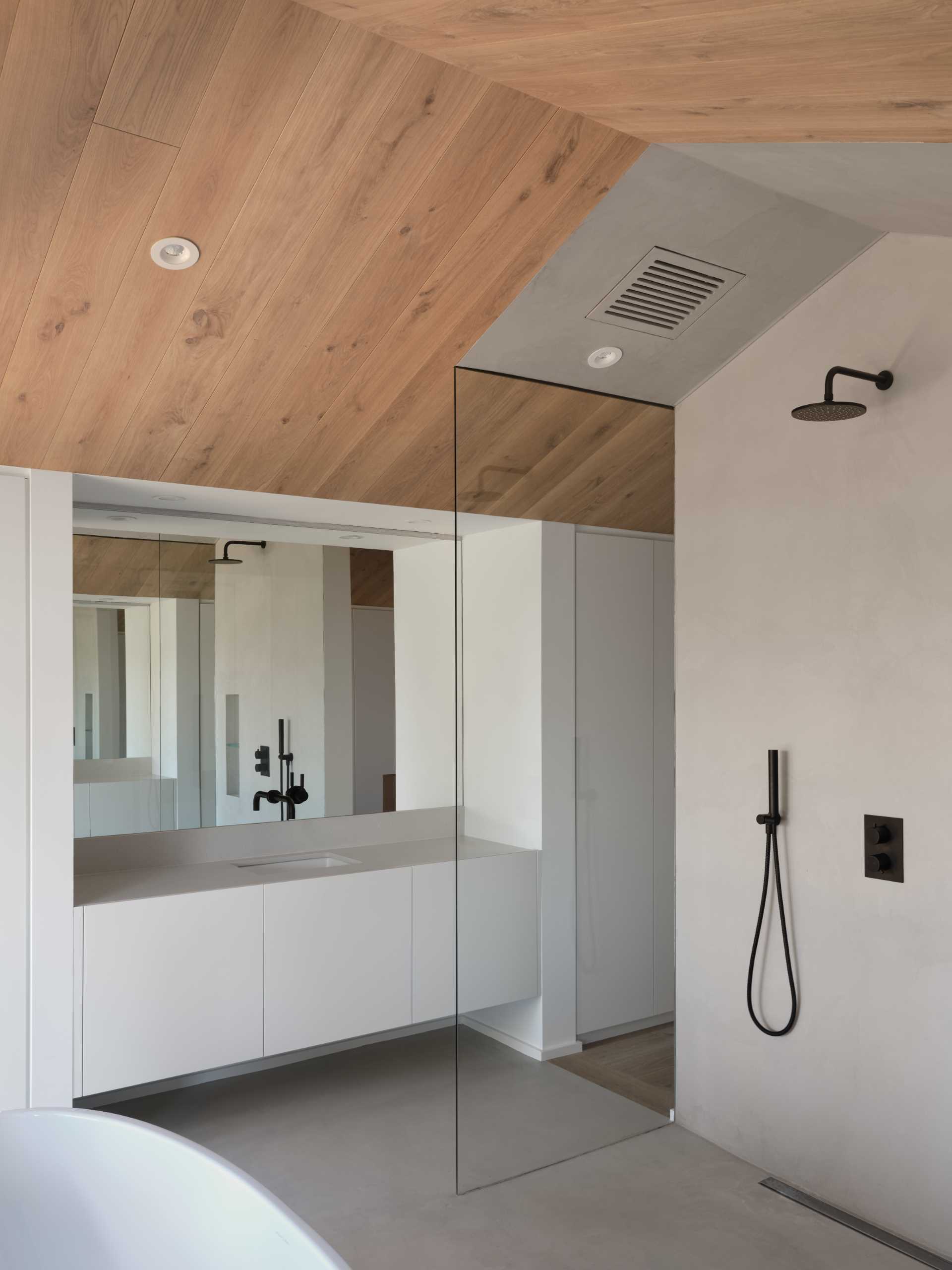 This primary bathroom has a walk-in s،wer and a large vanity with cabinetry on either side, while a freestanding bathtub is positioned by the window that looks out to a private deck.