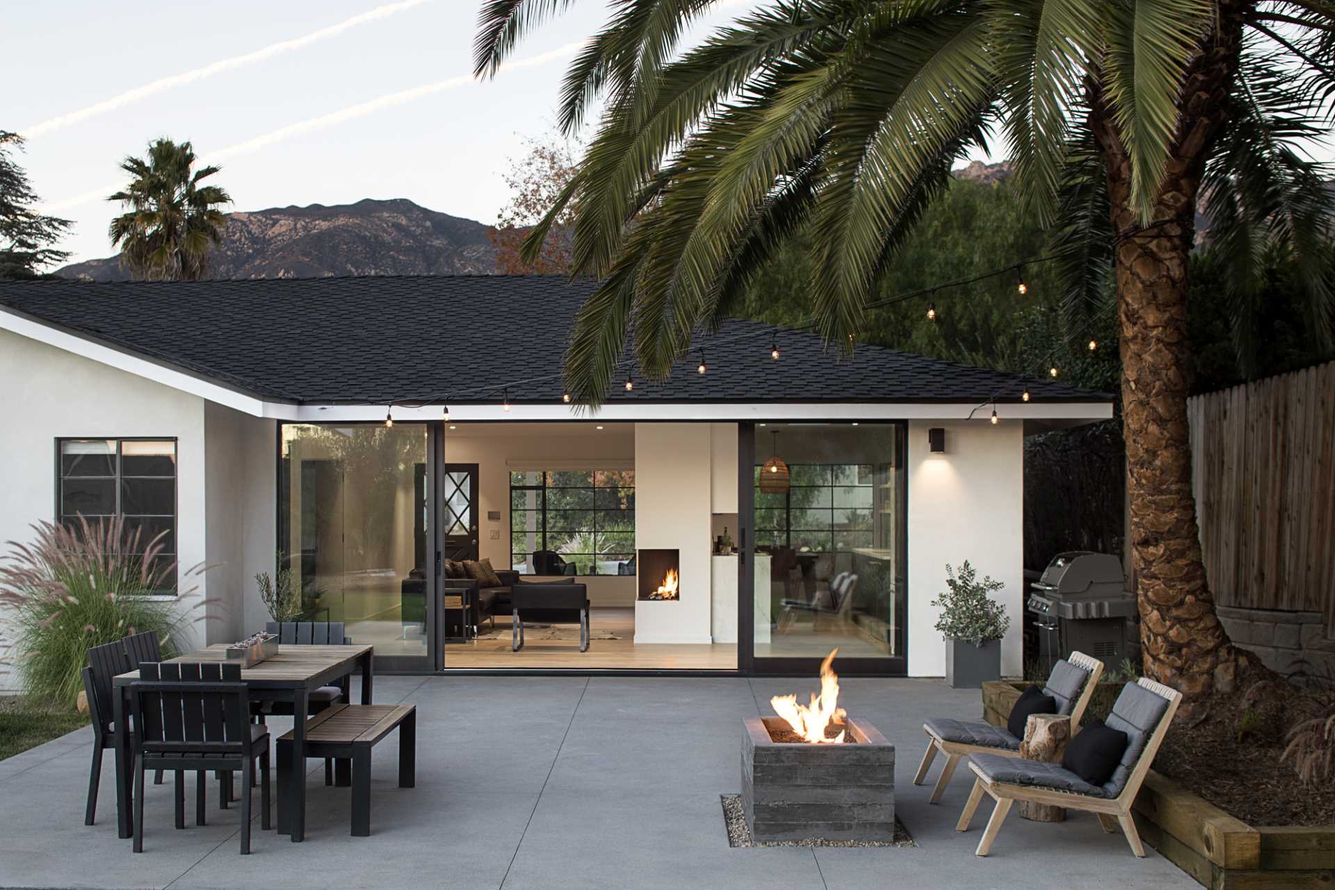 A new, large glass sliding wall now leads out to the rear yard, where there's a patio with outdoor dining, a BBQ, and a fire pit. String lights help to create an ideal outdoor entertaining area.