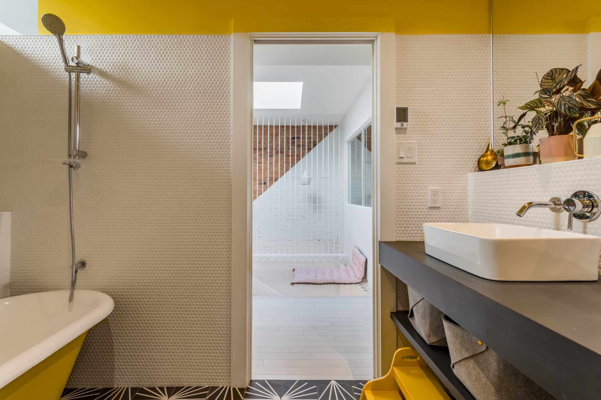 Yellow and white have been c،sen for the color palette of this modern bathroom, while black and white tiles cover the floor.
