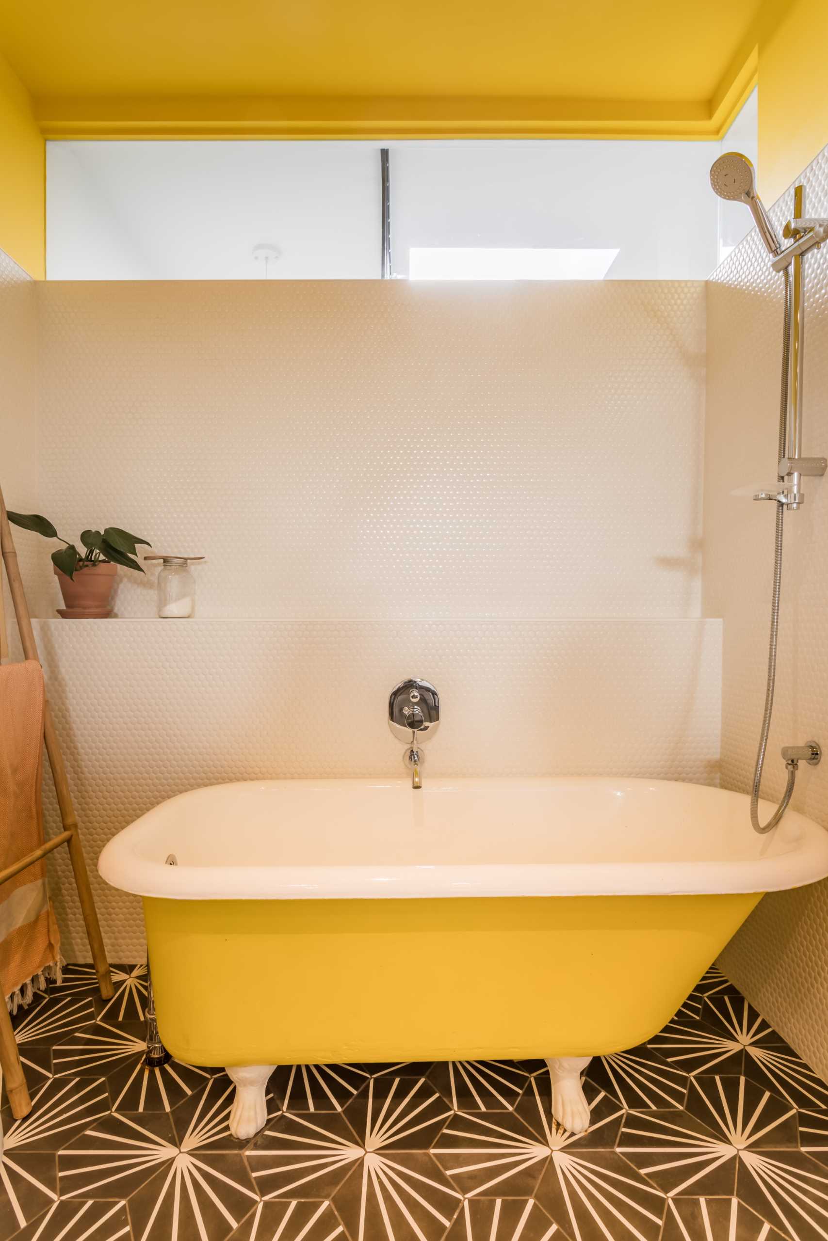 Yellow and white have been c،sen for the color palette of this modern bathroom, while black and white tiles cover the floor.