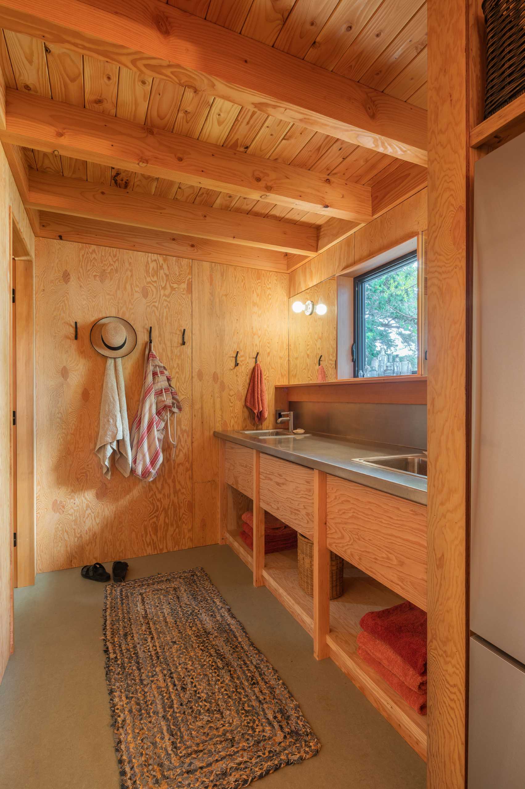 In the bathroom area of this cabin, there's a custom stainless steel counter with matching sinks, polished chrome faucets, and mirrors positioned on either side of the window.