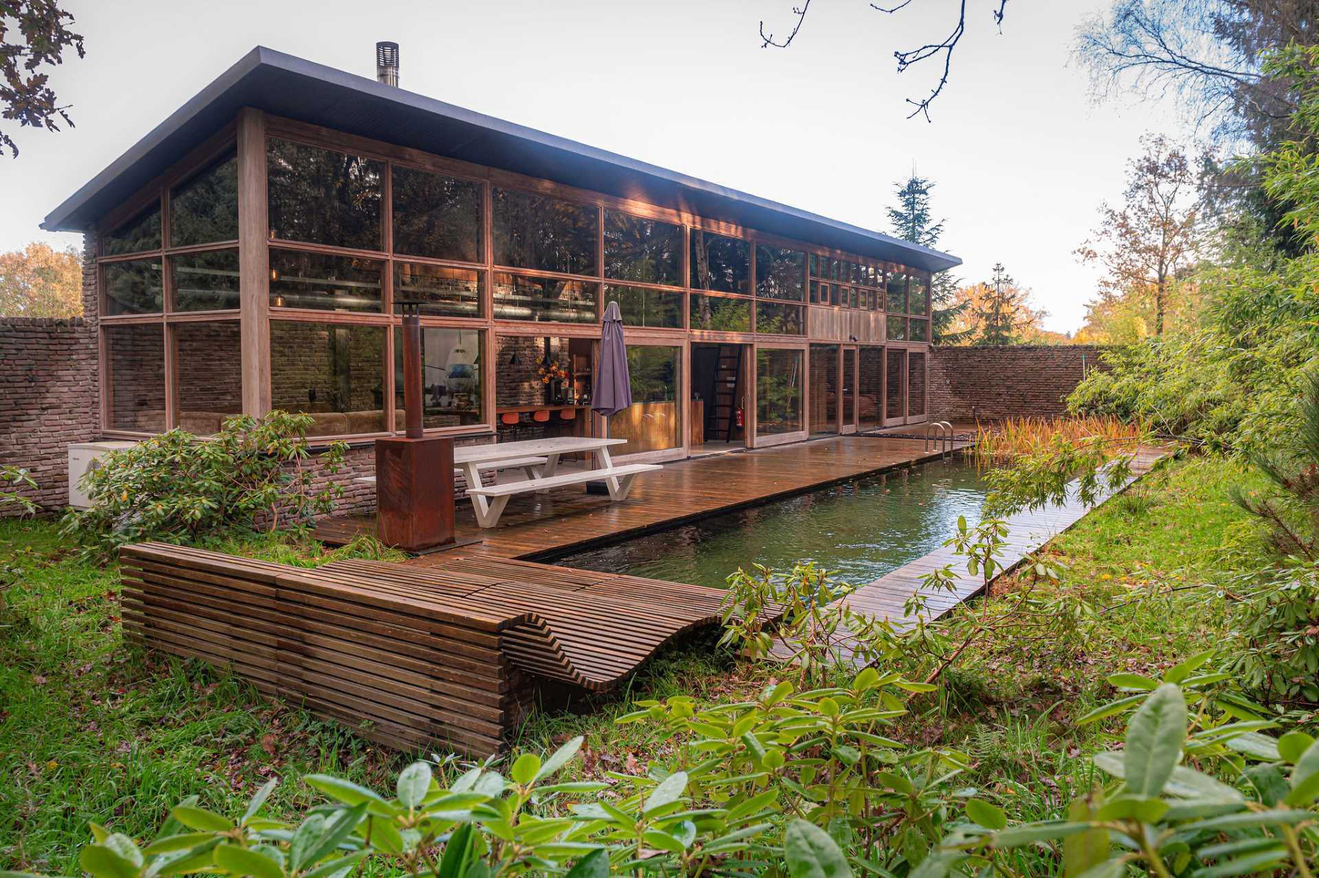 A modern home with rough and rugged materials like bricks and wood, also has a natural swimming pool.