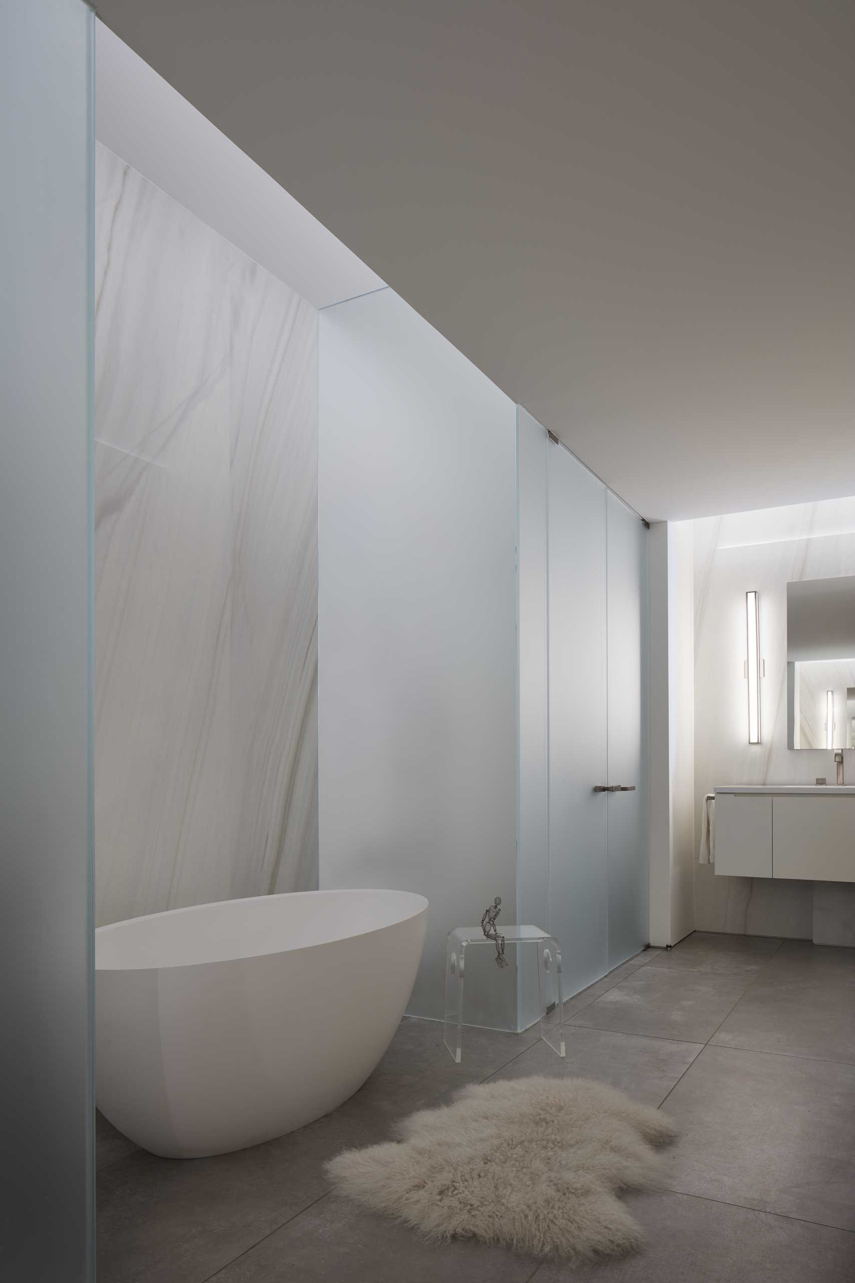 This bathroom has a freestanding bathtub, frosted glass walls, and a floating vanity.