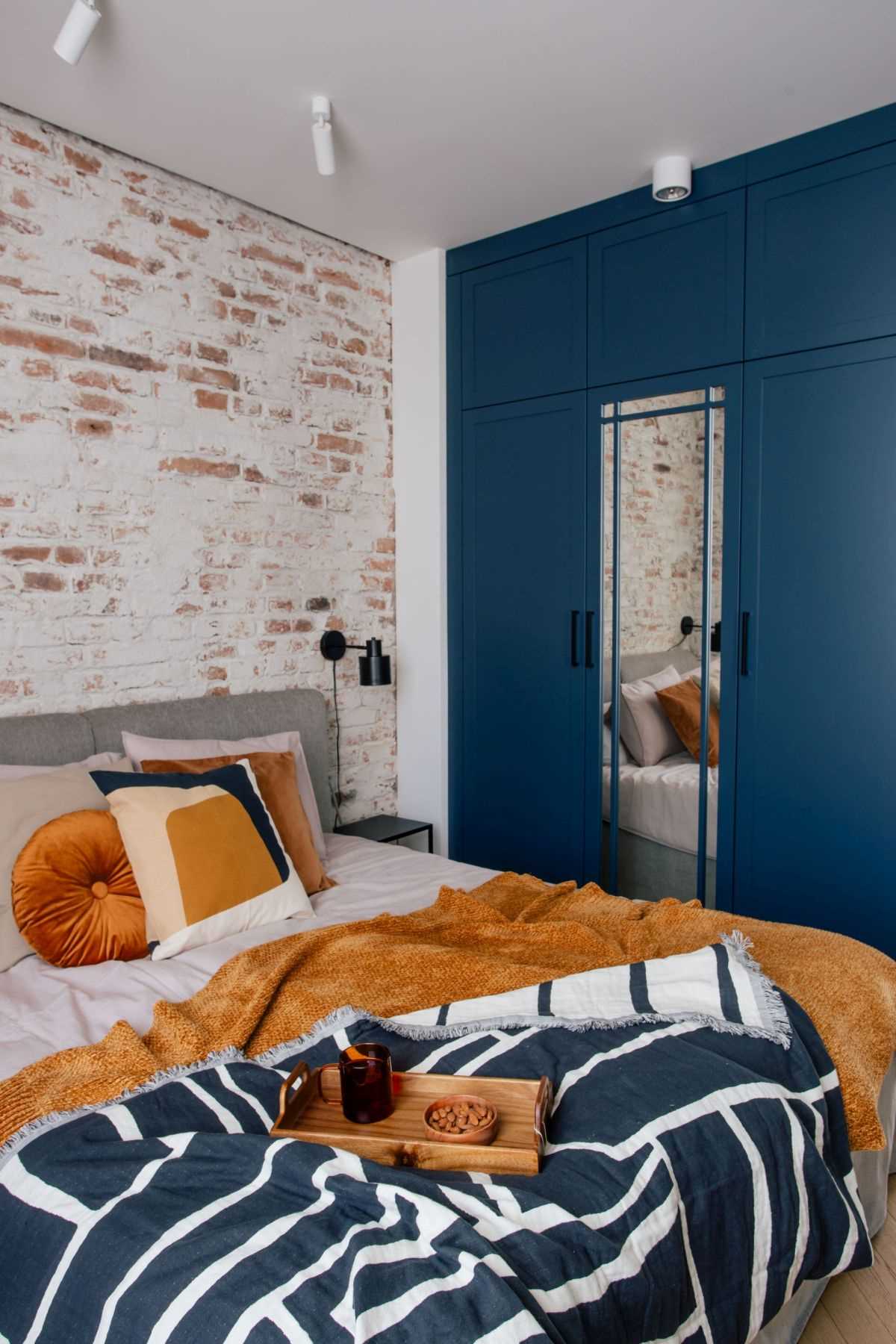 In this bedroom, the brick wall is structural and was exposed to act as an accent wall. Deep blue cabinetry has been built around a mirror.