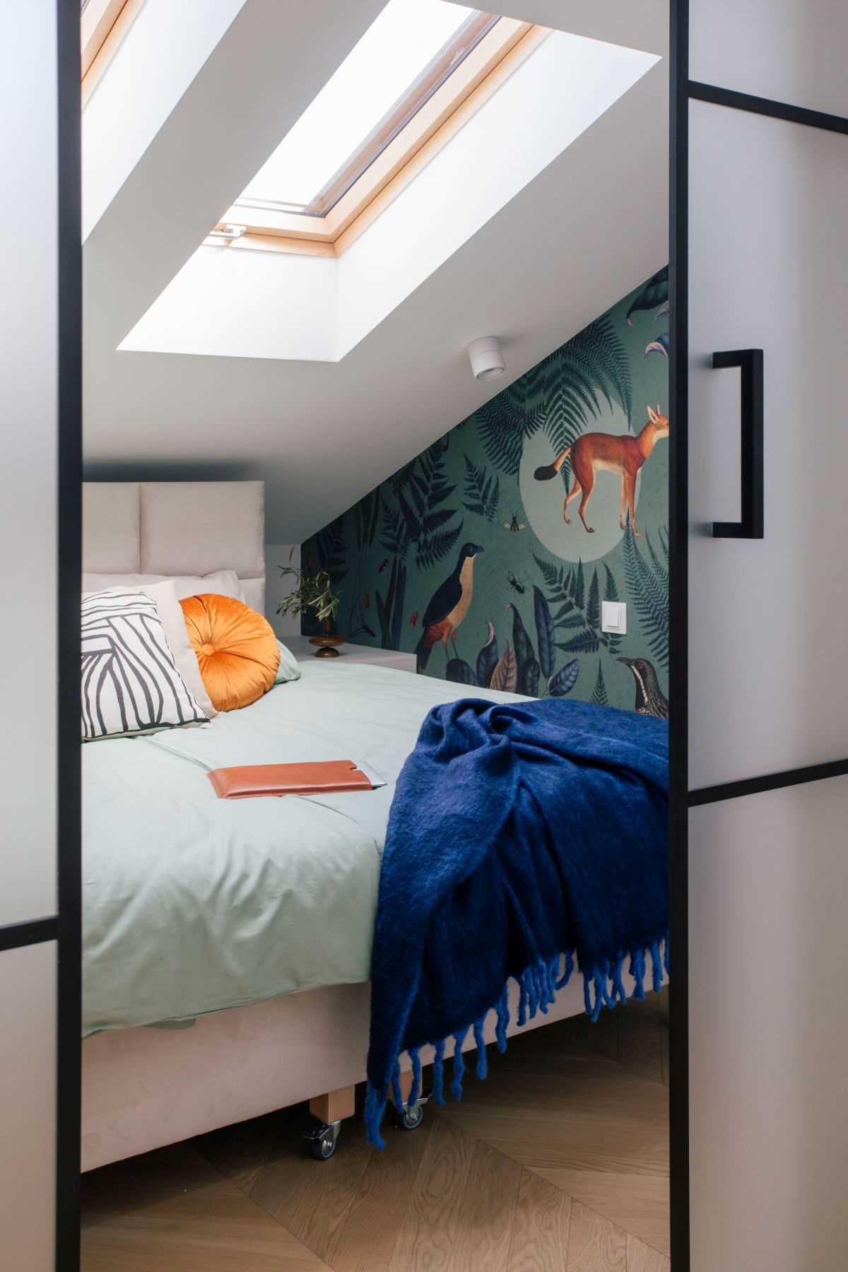 In this modern bedroom, there's multiple skylights and a wallpaper with botanicals, birds, and animals.