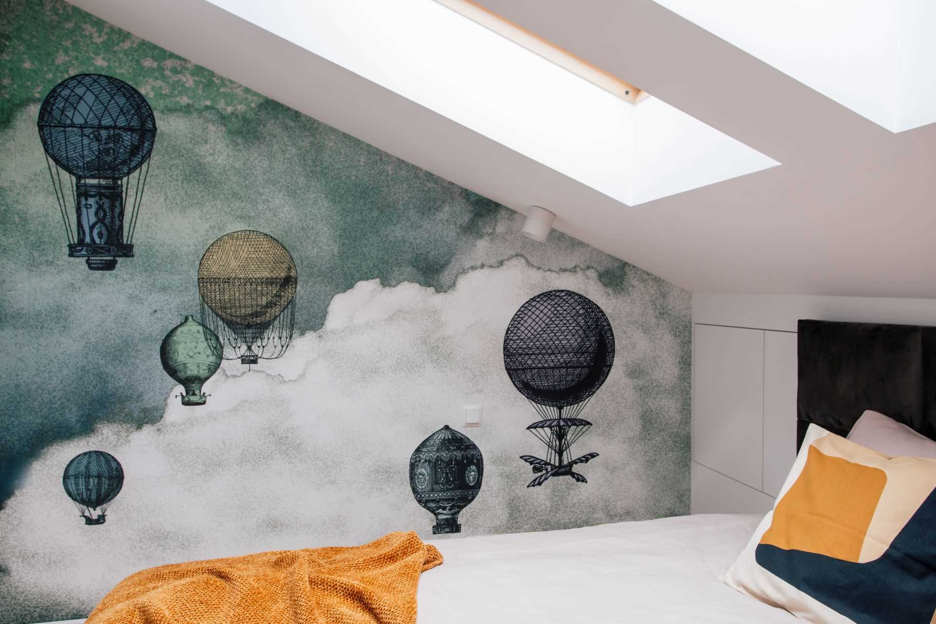 In this modern bedroom, there's multiple skylights, a built-in bench, and a wallpaper with a hot air balloon print.
