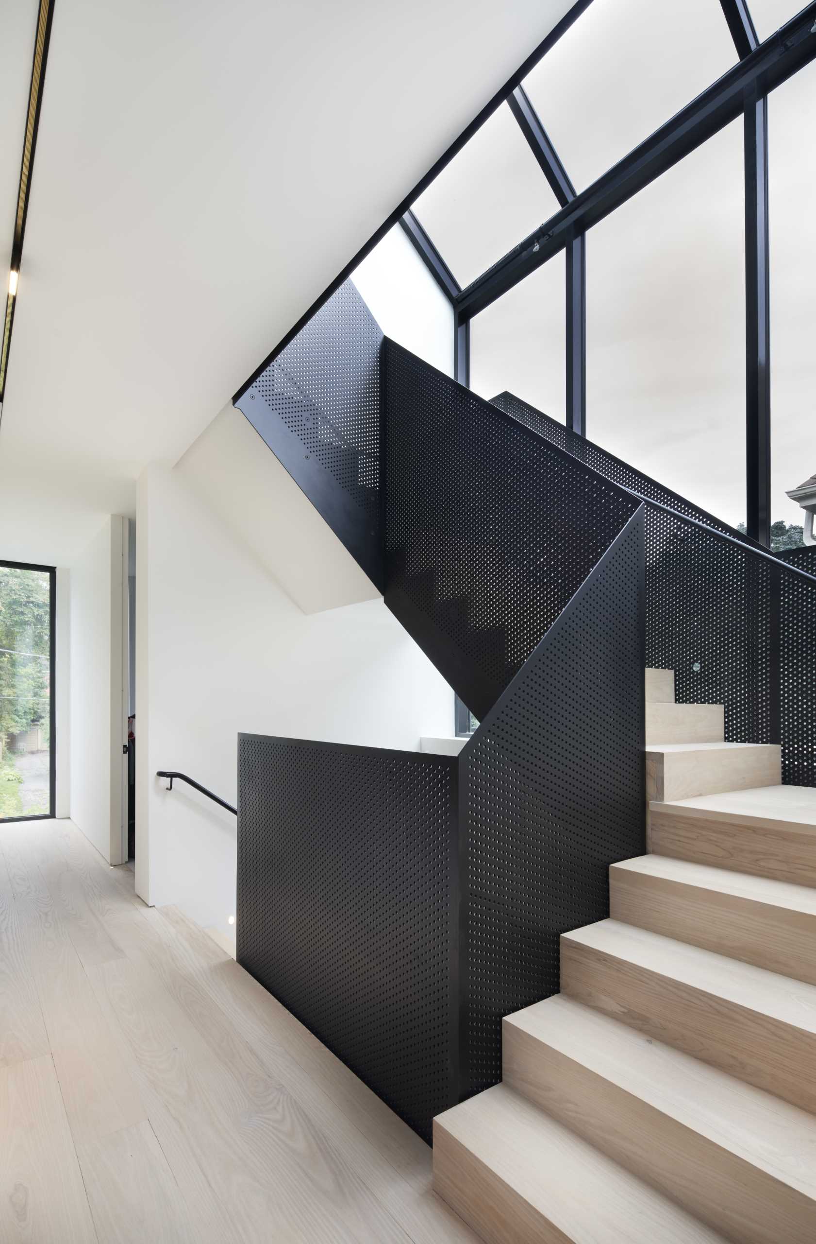 Wood stairs with perforated black metal railings connect the multiple levels of the home 