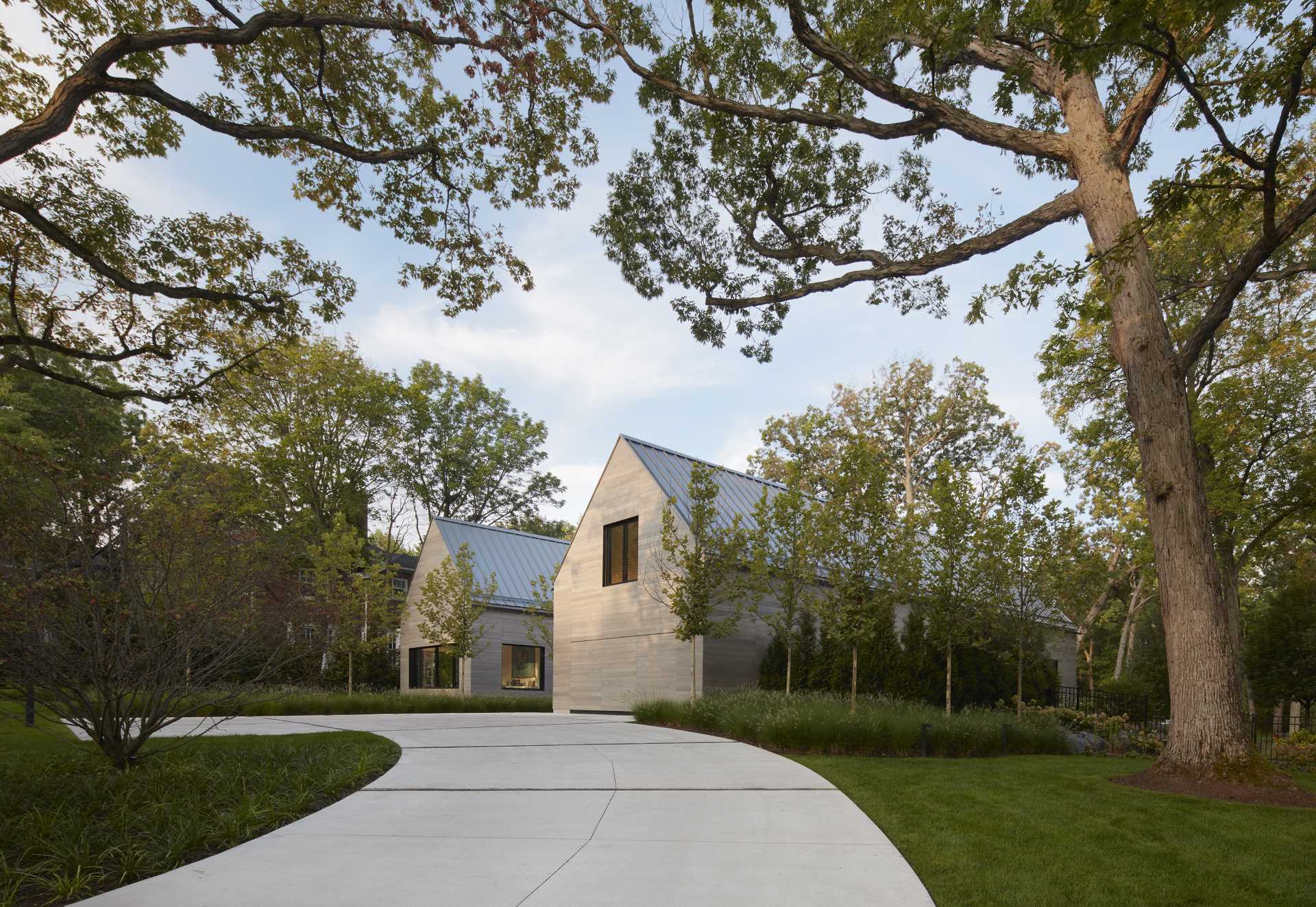 The exterior of this modern home with two gables, is composed of warm gray Accoya siding, deeply inset windows, and zinc-colored standing seam roofing. 