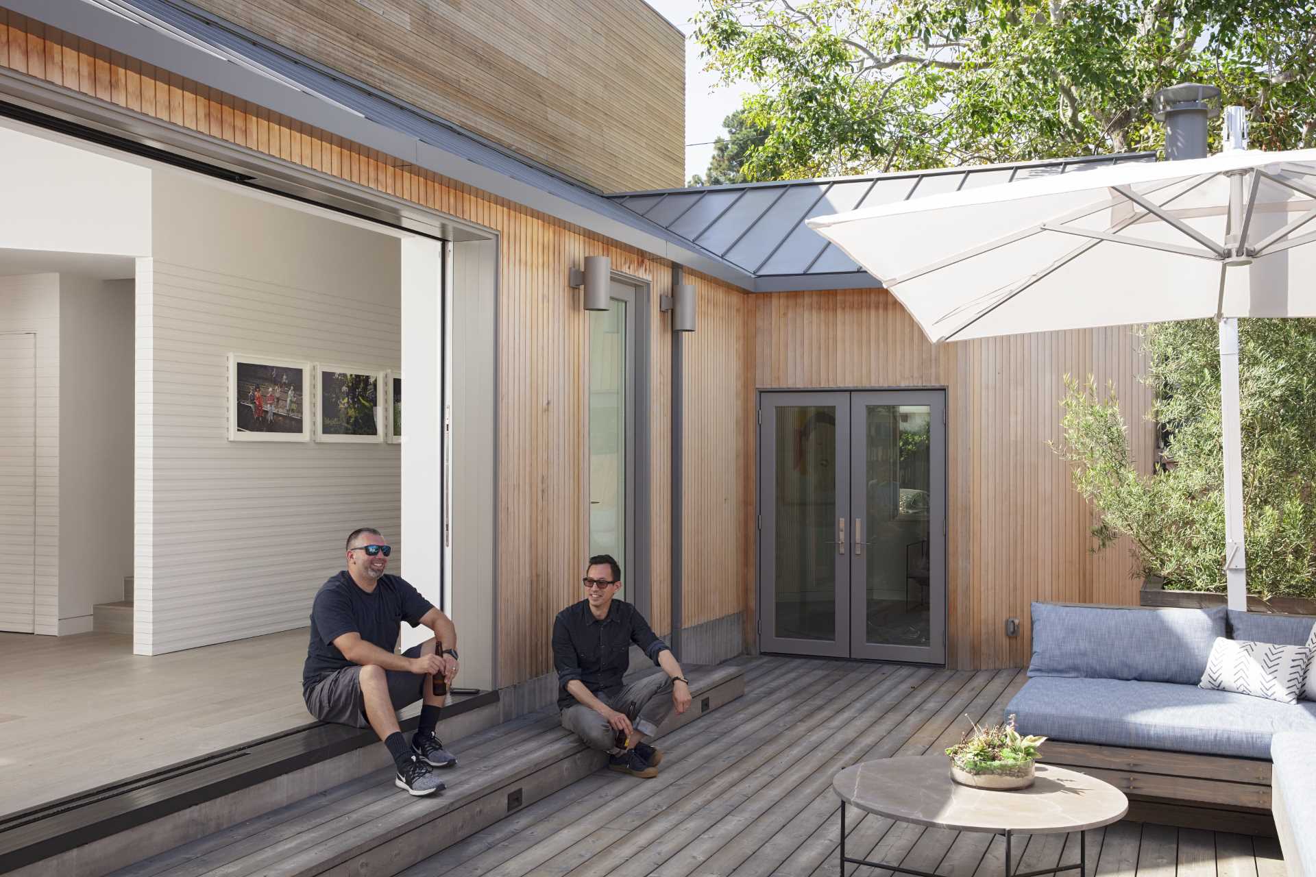 A modern house with wood siding, has large sliding doors that open to the patio.