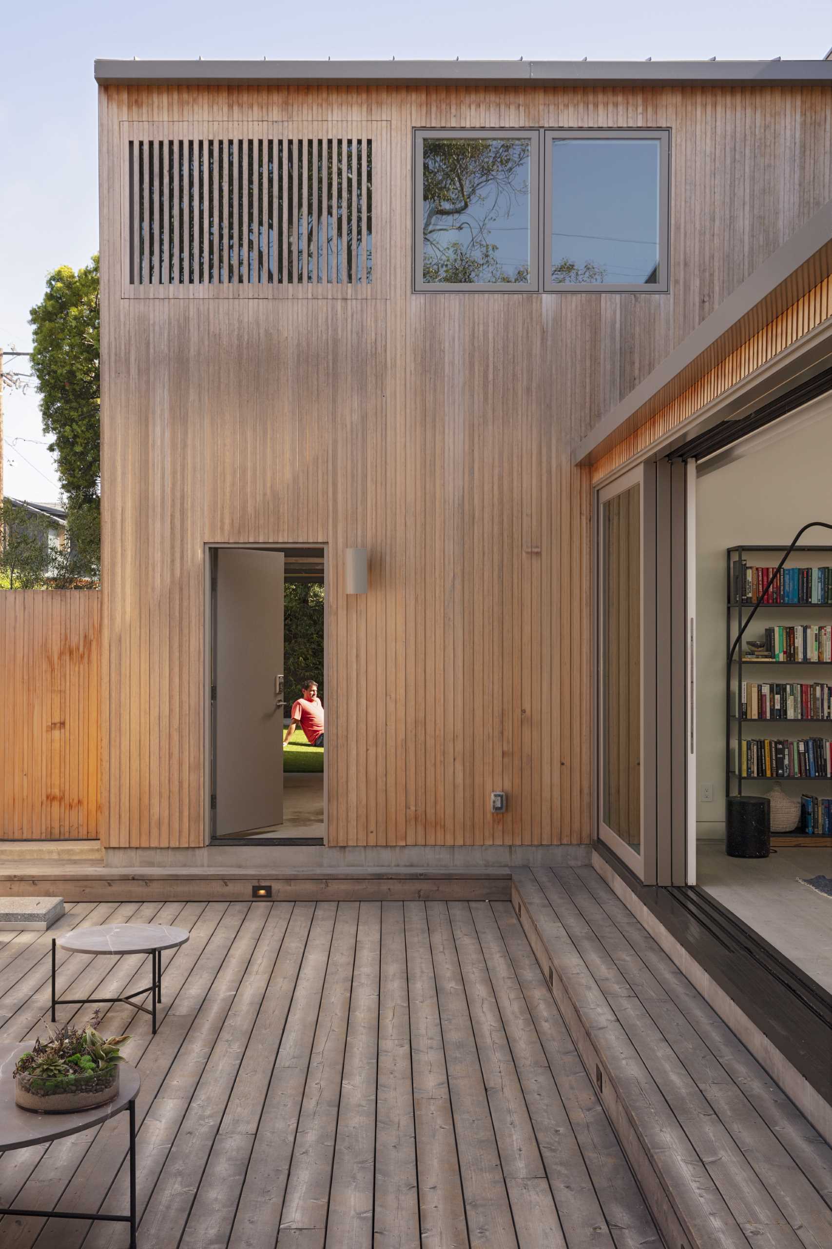 A modern house with wood siding, has large sliding doors that open to the patio.