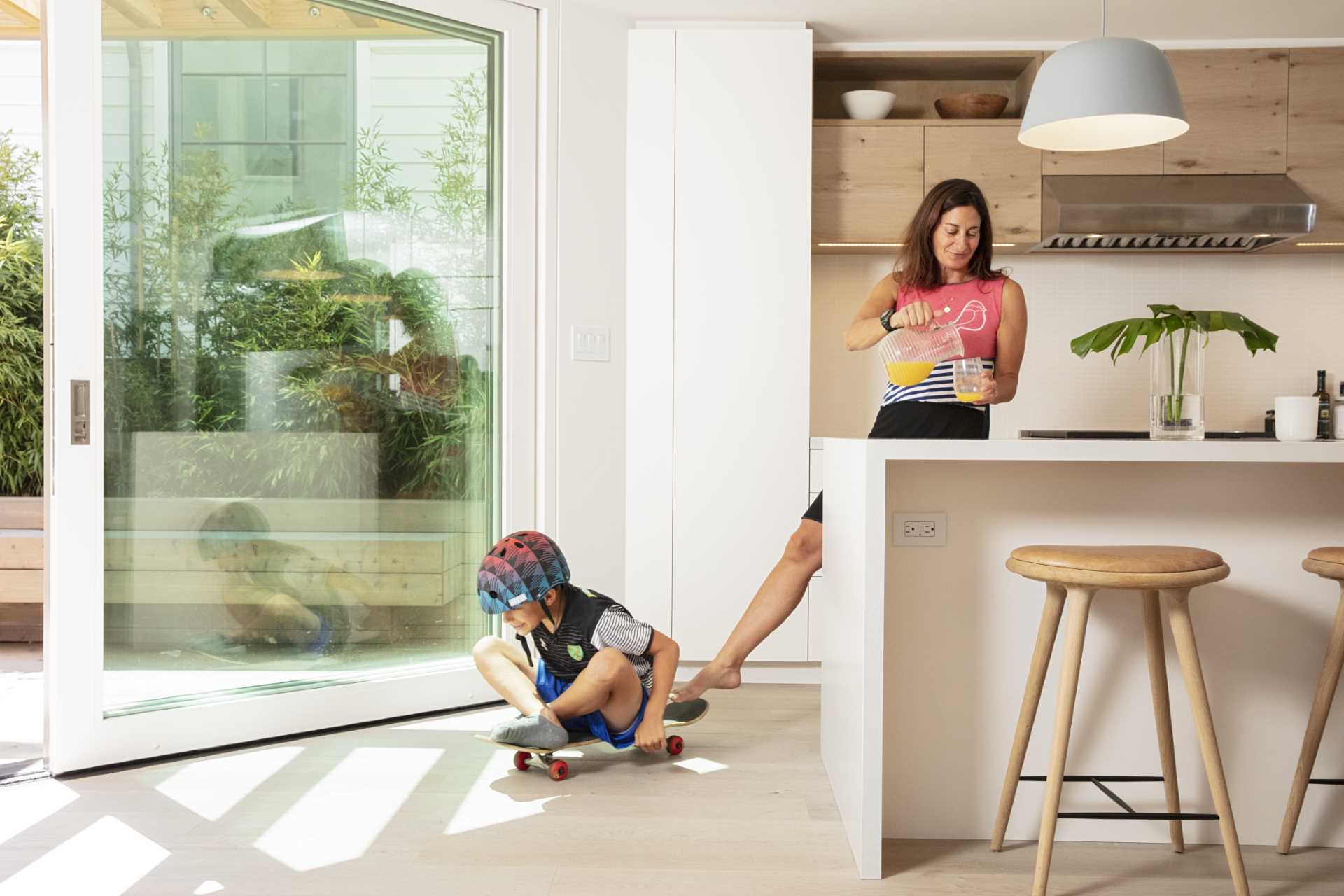 This modern kitchen, with its white and wood cabinetry, and white island, has a sliding glass door that connects with the outdoor space.