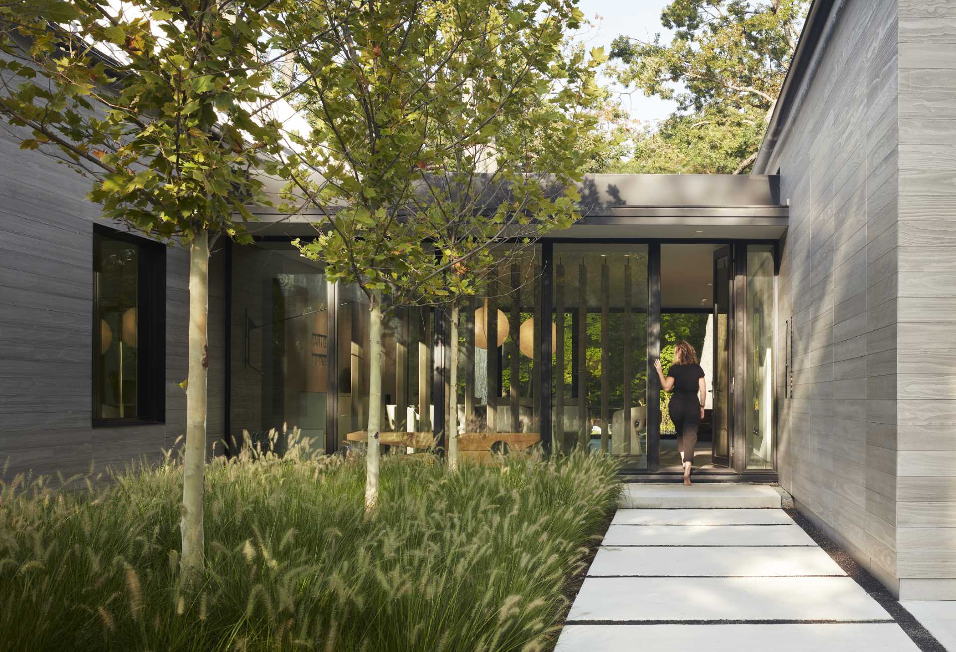 The exterior of this modern home with two gables, is composed of warm gray Accoya siding, deeply inset windows, and zinc-colored standing seam roofing. 