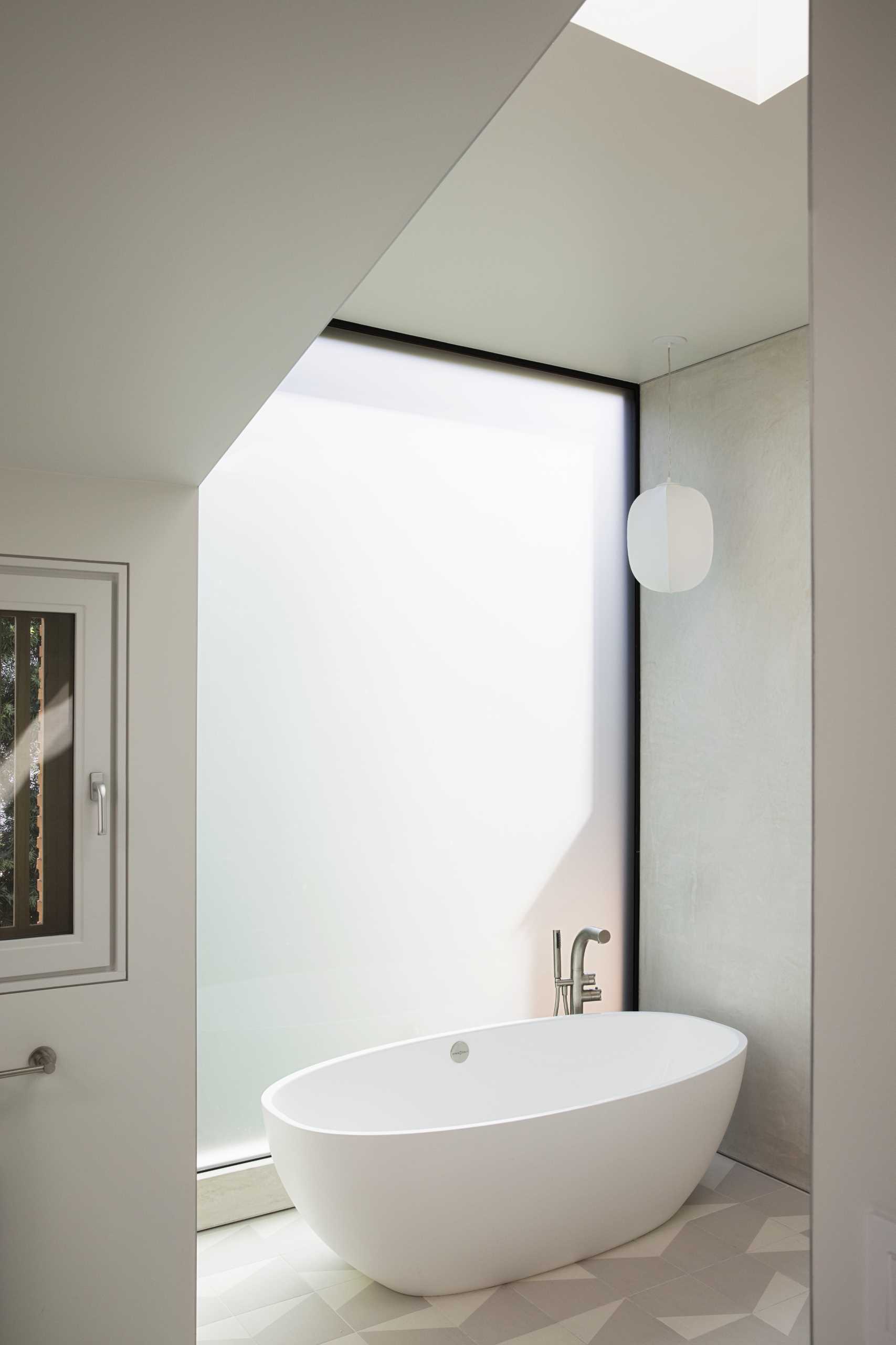 In this primary bathroom, the freestanding bathtub is positioned in front of the large window, while a secondary window by the vanity has wood slats providing privacy even when the window is open.