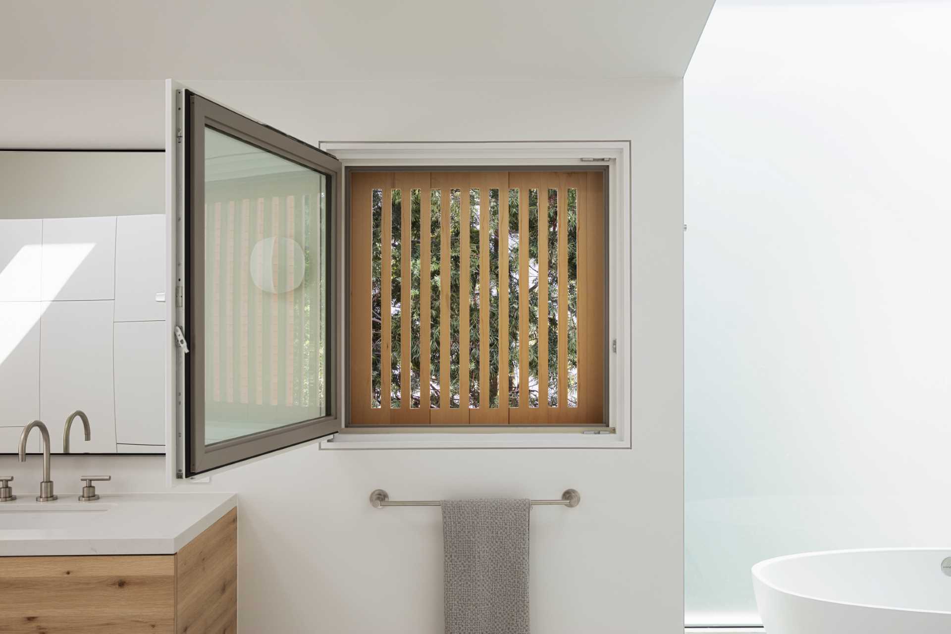 In this primary bathroom, the freestanding bathtub is positioned in front of the large window, while a secondary window by the vanity has wood slats providing privacy even when the window is open.