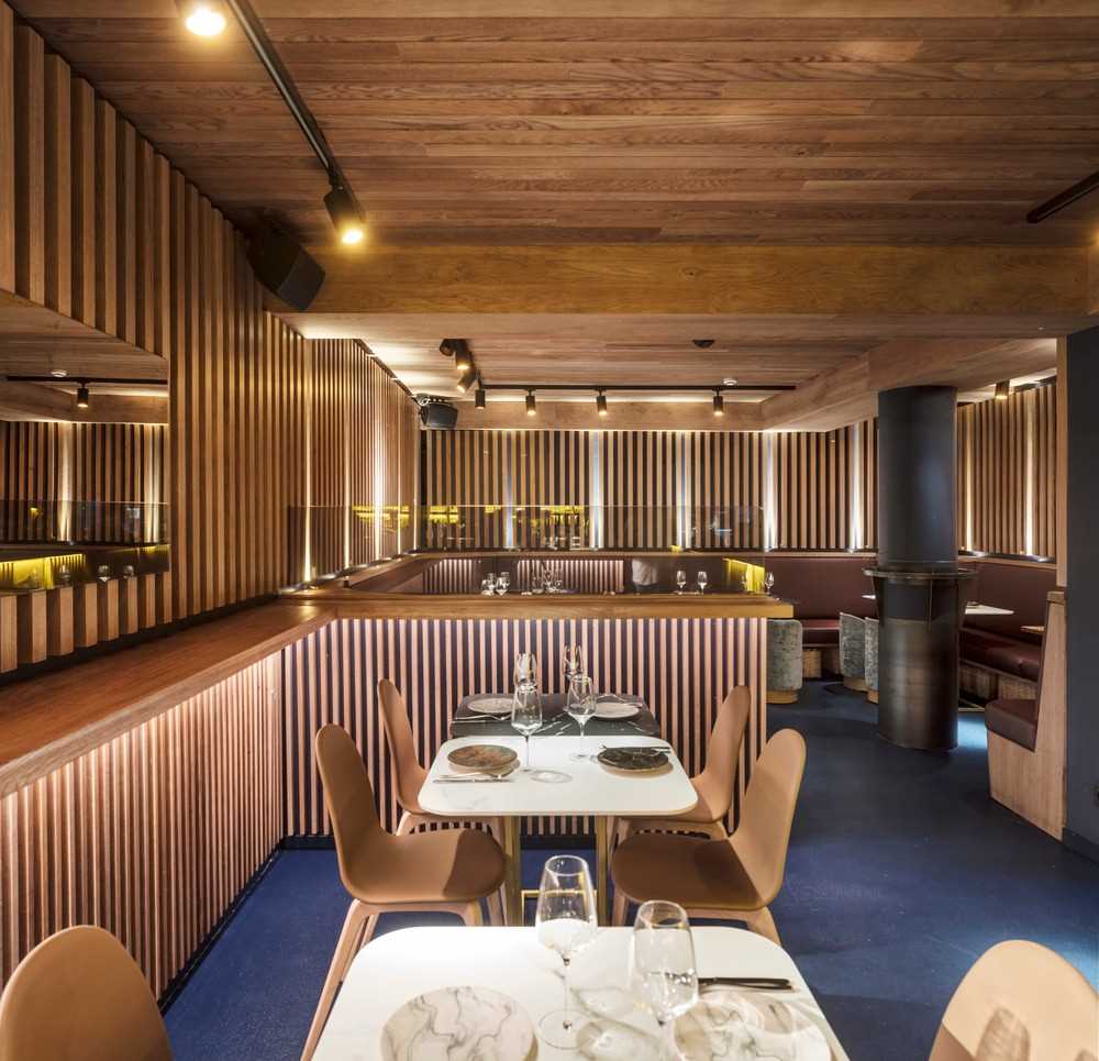 The design of this restaurant basement was inspired by an old boat cellar where the warm golden wood-tones surround the customers, in contrast to the blue maritime floor.