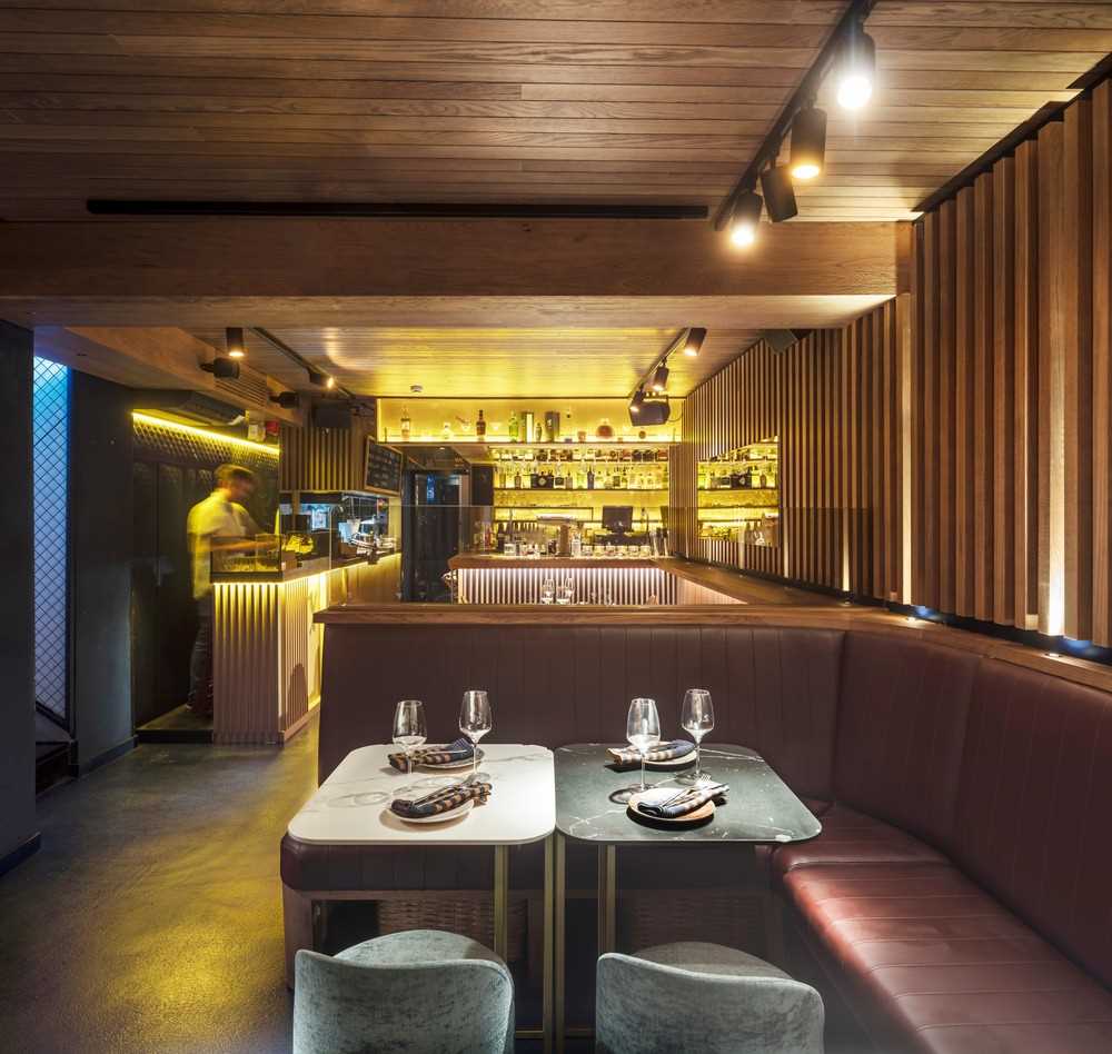 The design of this restaurant basement was inspired by an old boat cellar where the warm golden wood-tones surround the customers, in contrast to the blue maritime floor.